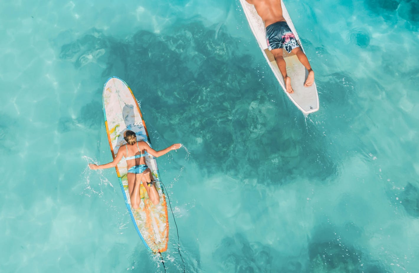 Two people in the ocean laying on surf boards, paddling out to catch a wave.