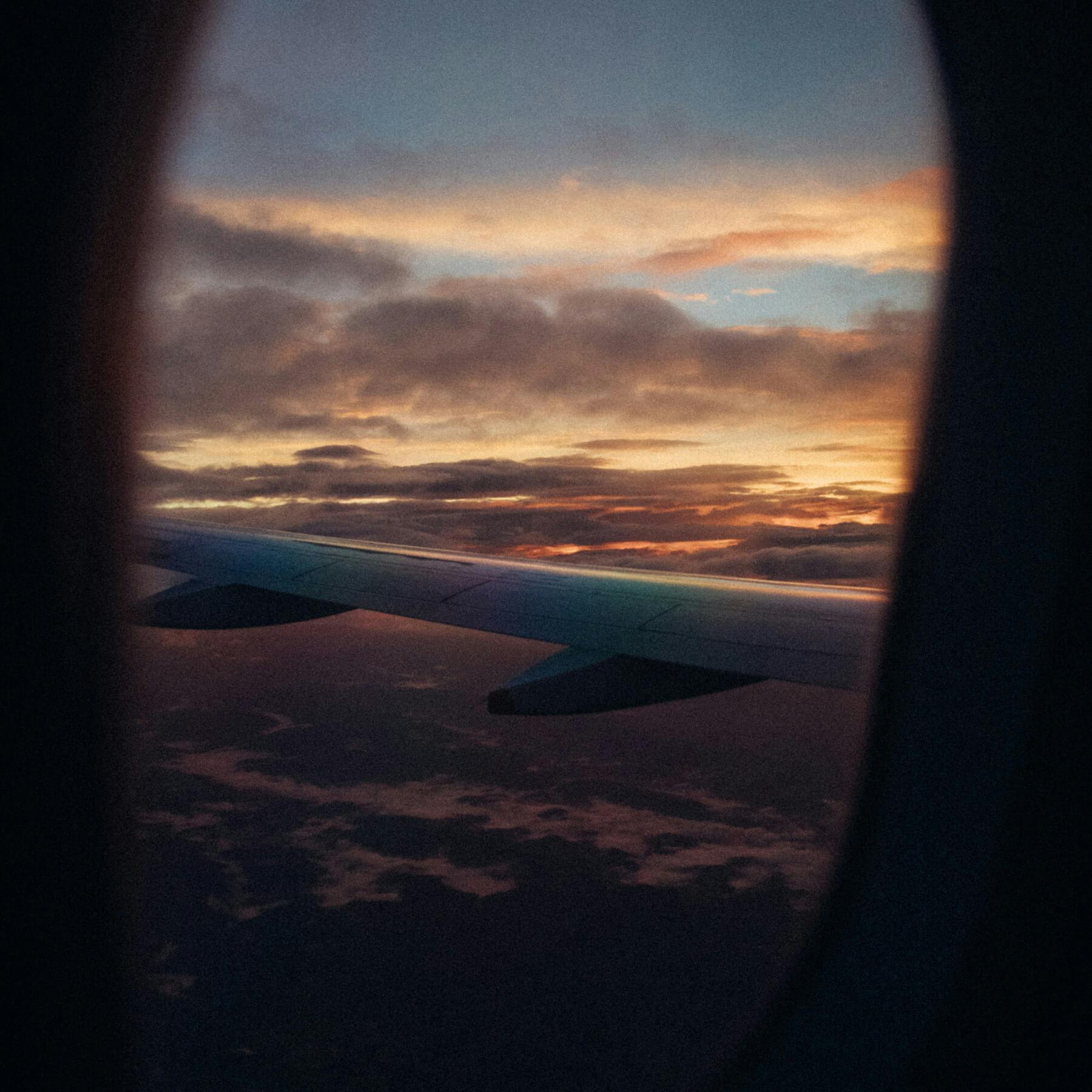 Looking out from the perspective of inside an airplane in flight looking at the plane's wing and the sunset.