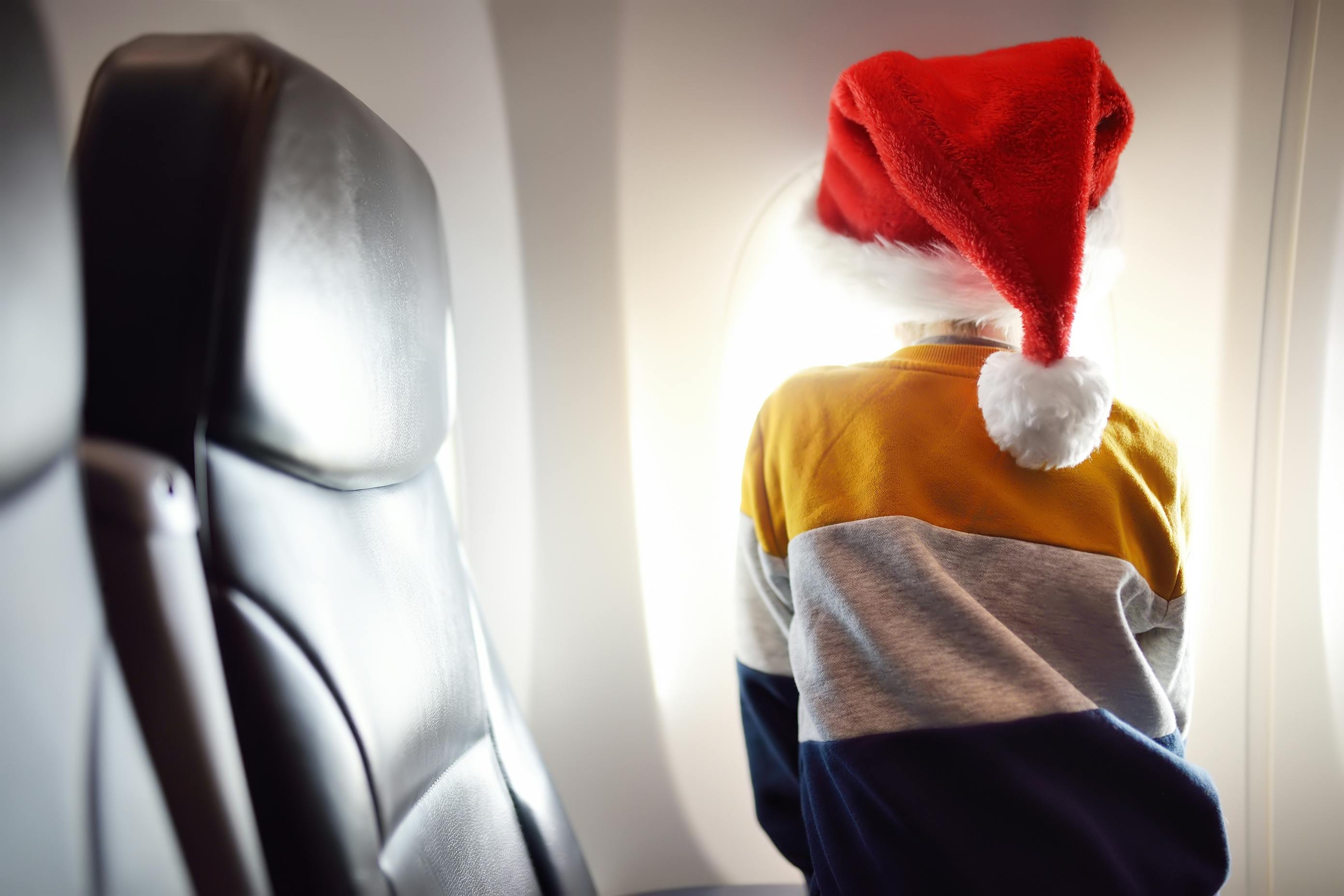 Child with santa hat looking outside plane window