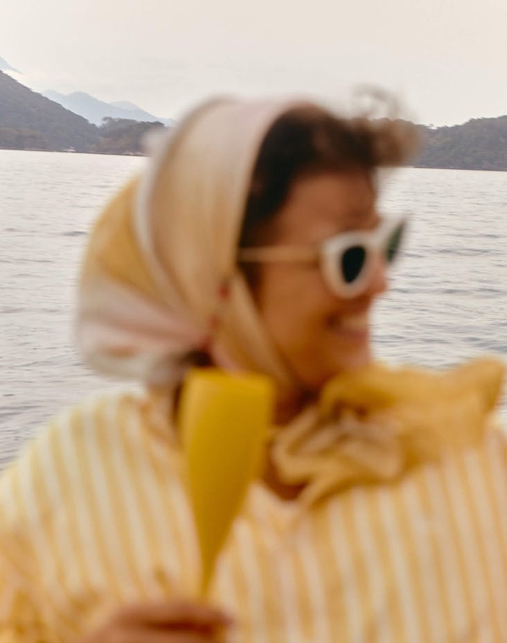 Blurred image of a woman on the water with a scarf in her hair. She holds a modern, yellow champagn flute.