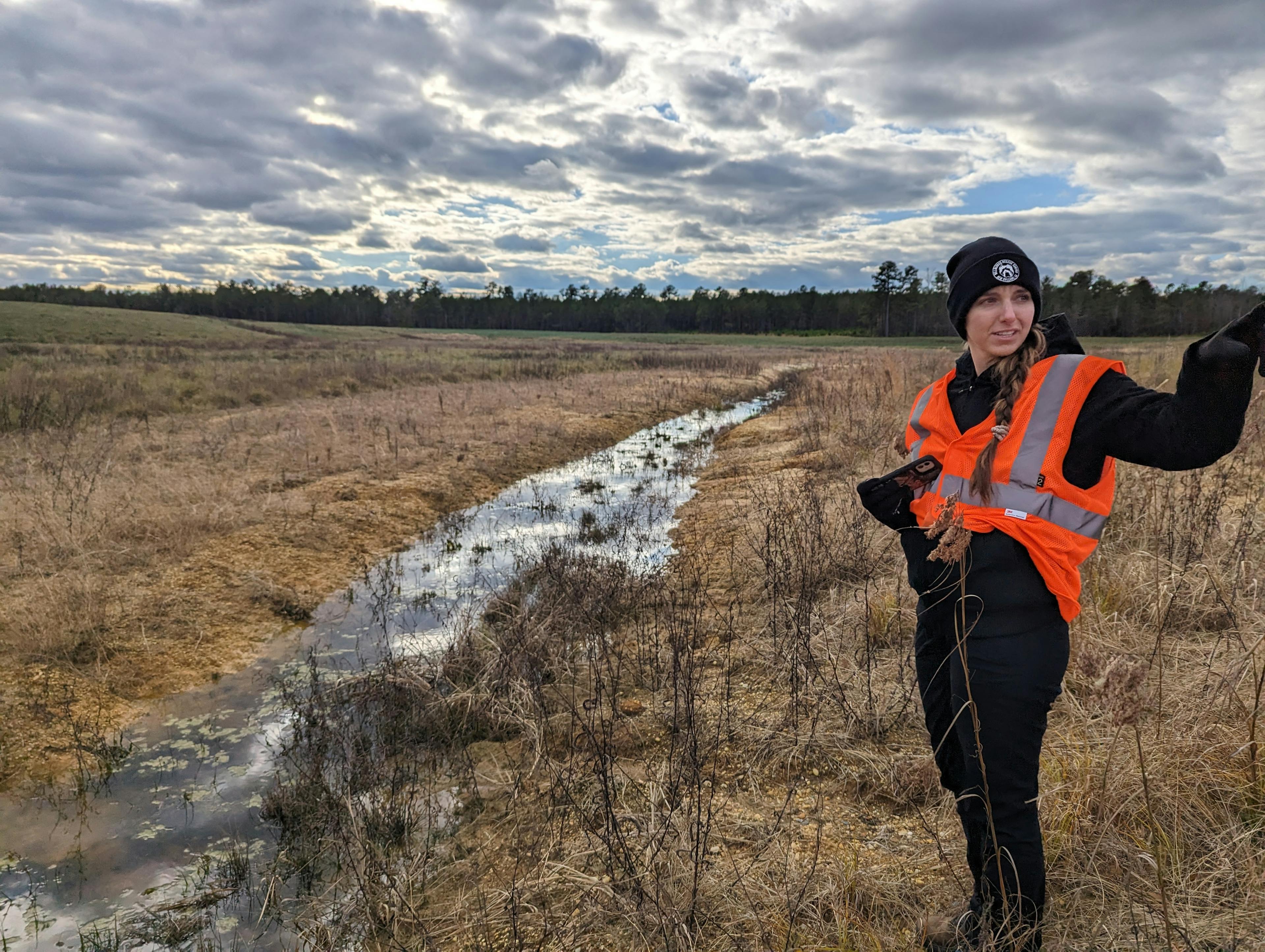 woman in hazard jacket pointing by a river