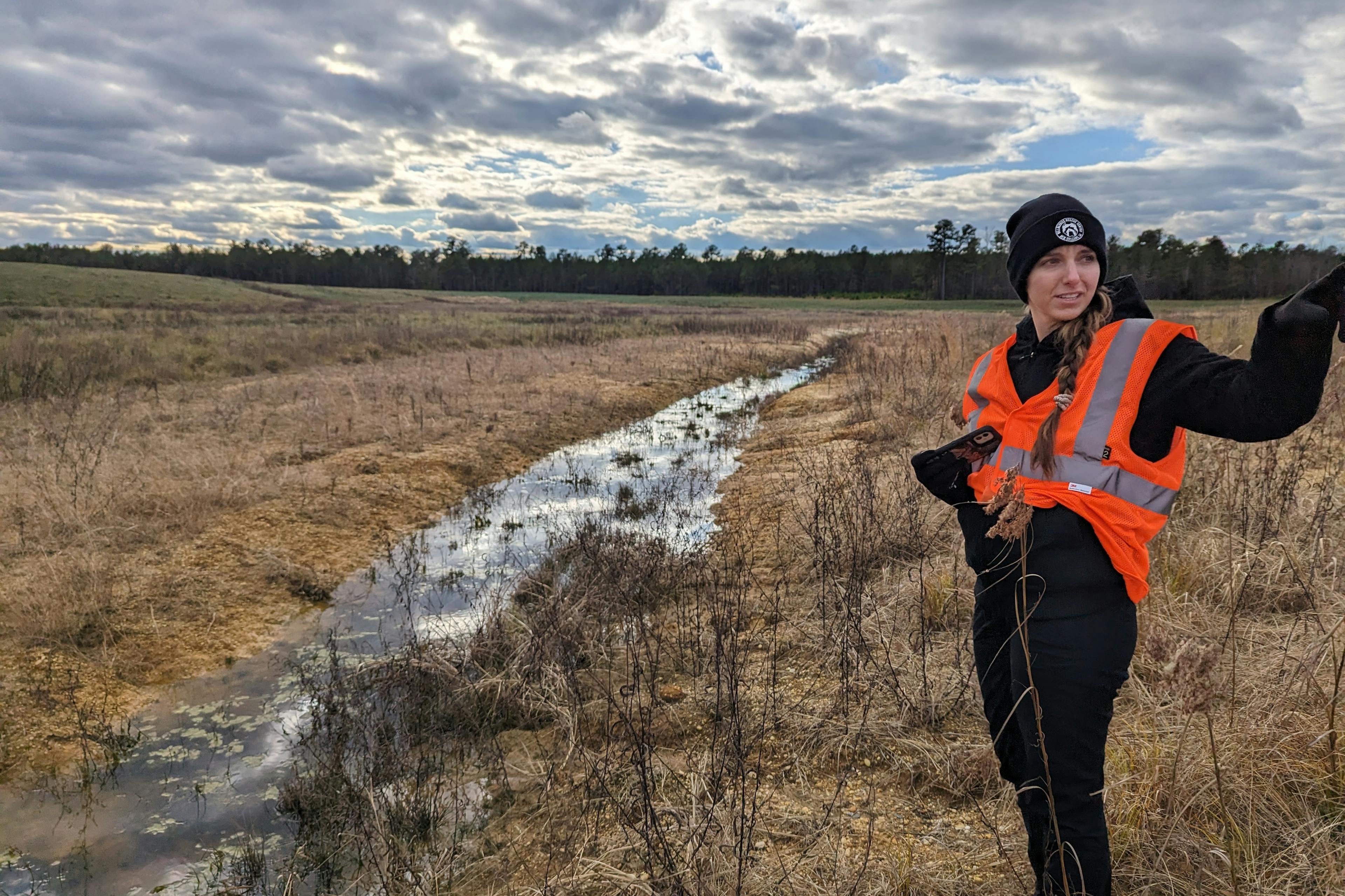 woman in hazard jacket pointing by a river