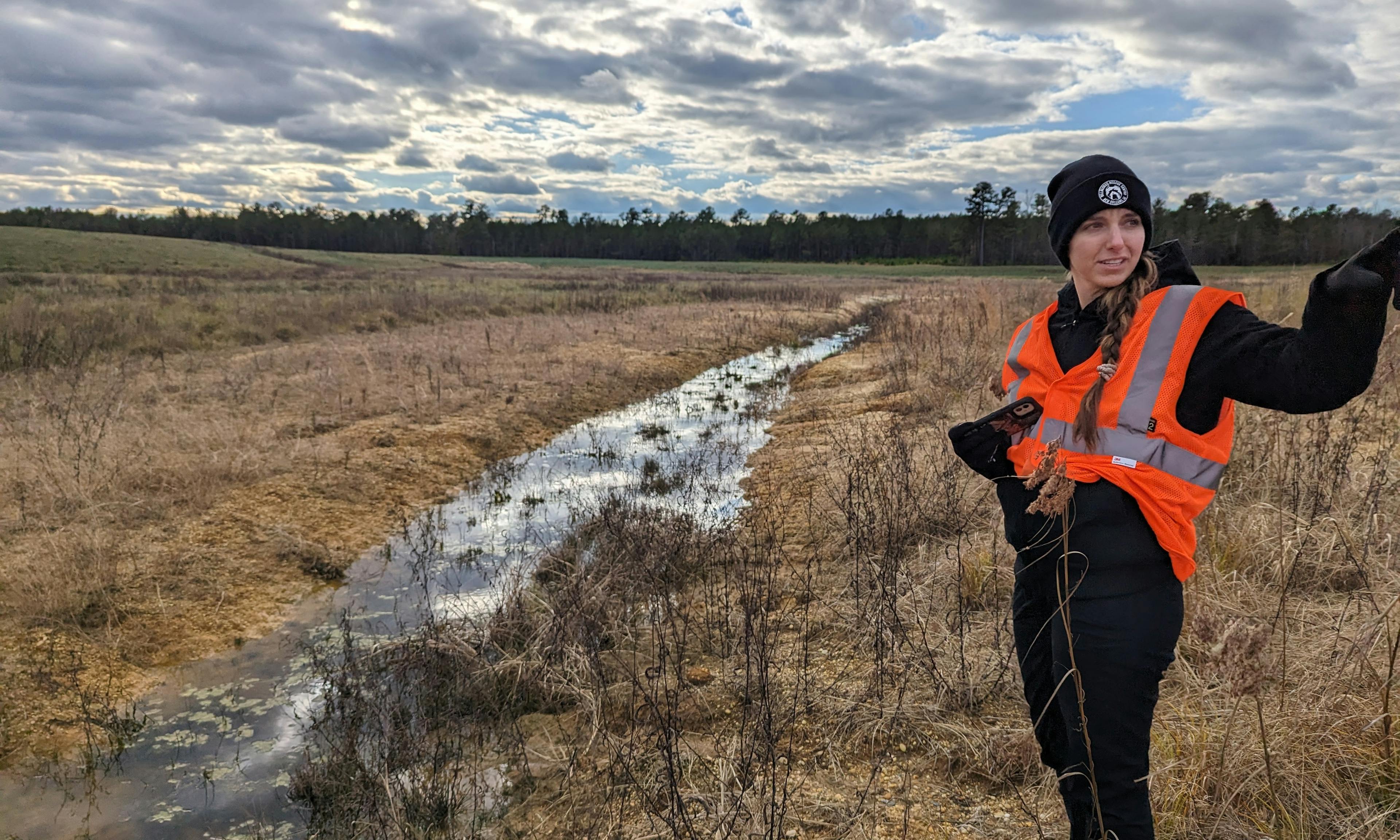 woman in hazard jacket pointing by a river