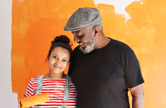 Senior man with daughter standing in front of a wall that they’re painting orange. 