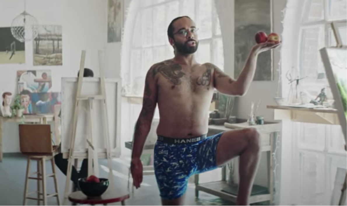 A man wearing underwear and holding apples shows body self-confidence while posing for artists.