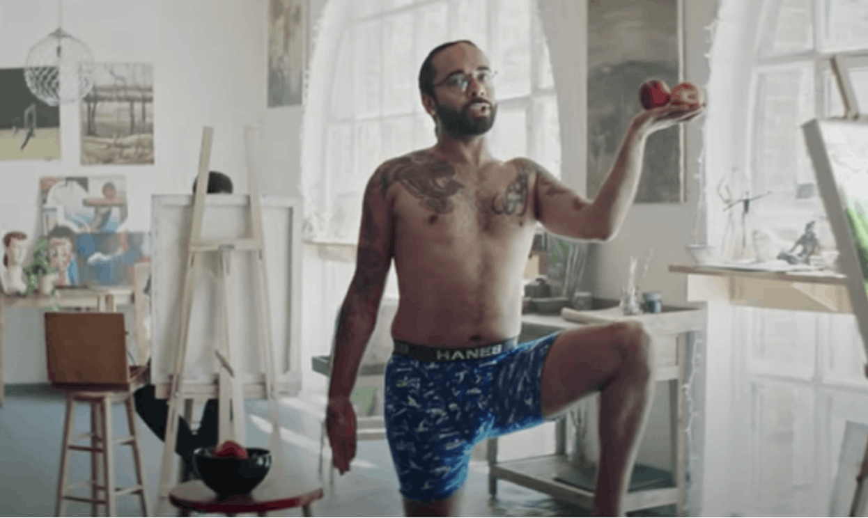 A man wearing underwear and holding apples shows body self-confidence while posing for artists.