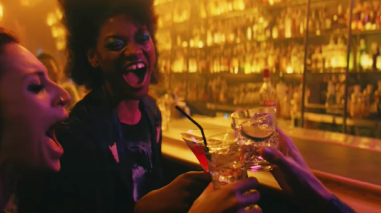 Three women laughing and celebrating with cocktails in a bar.