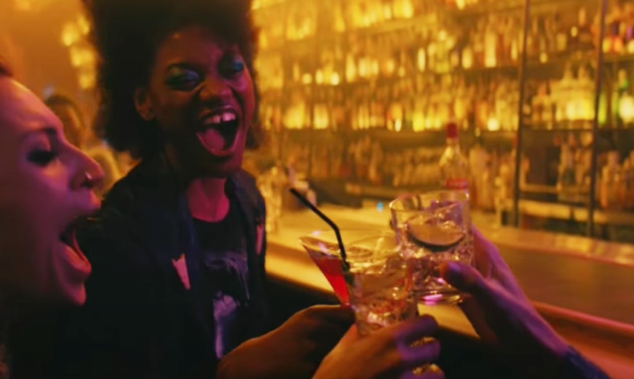 Three women laughing and celebrating with cocktails in a bar.