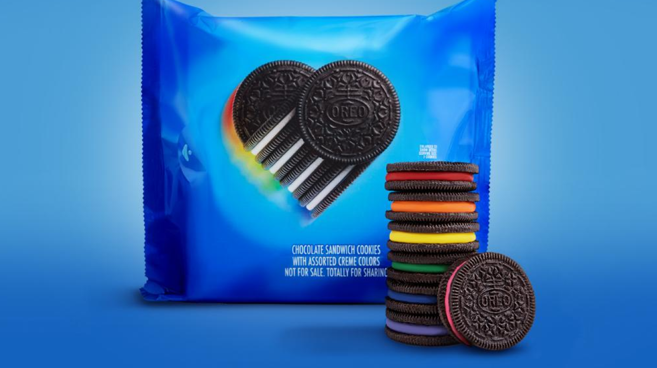 Oreo cookies with rainbow-colored creme centers are stacked in front of Pride-themed Oreo packaging.