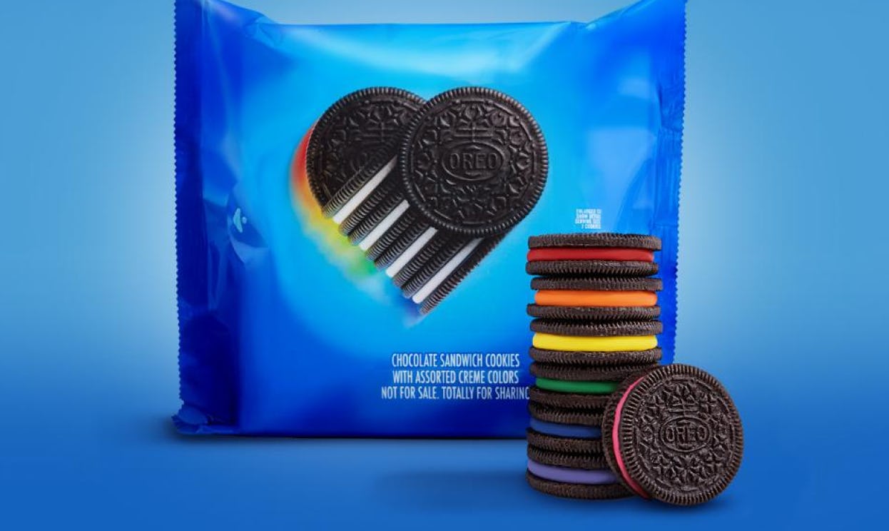 Oreo cookies with rainbow-colored creme centers are stacked in front of Pride-themed Oreo packaging.