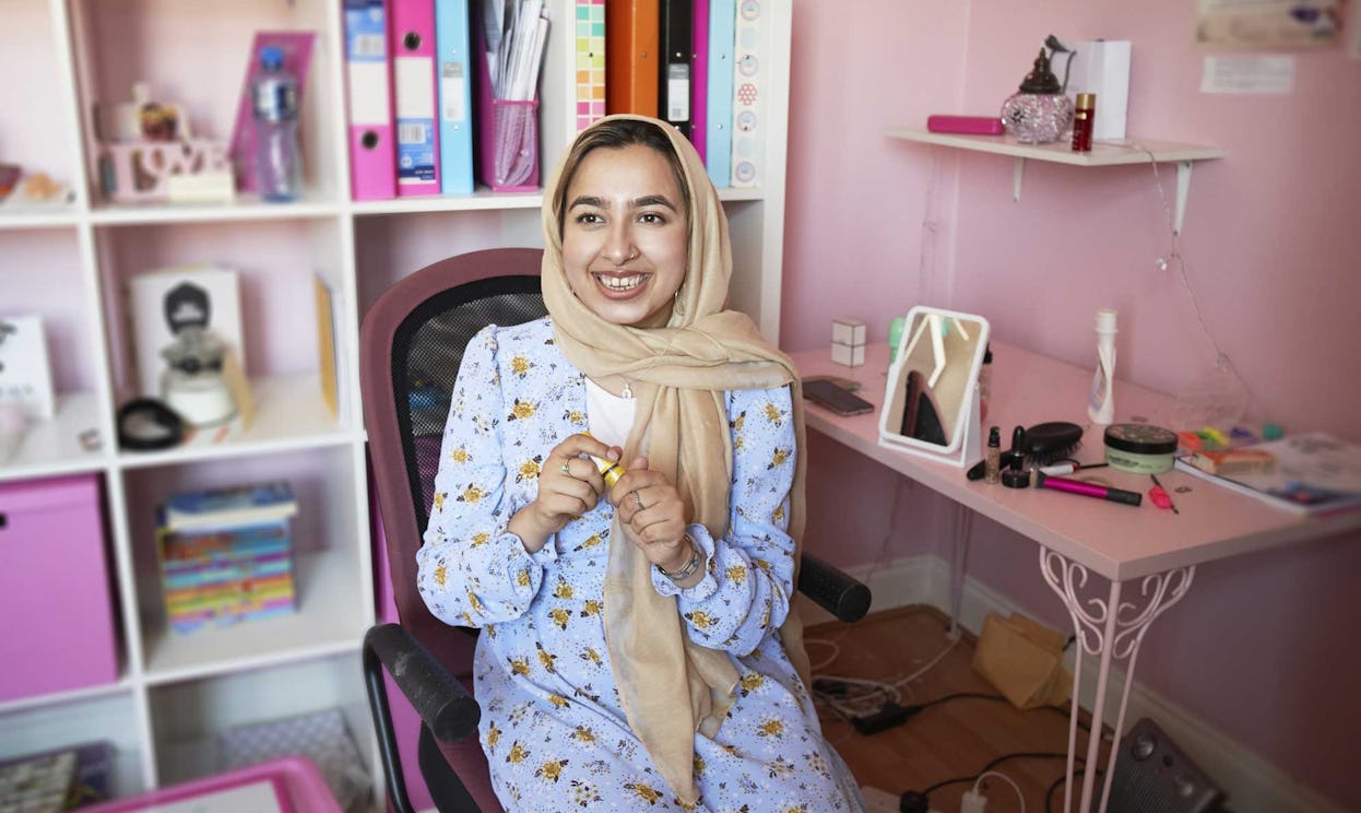 Young Muslim woman prepares her makeup in a pink room.