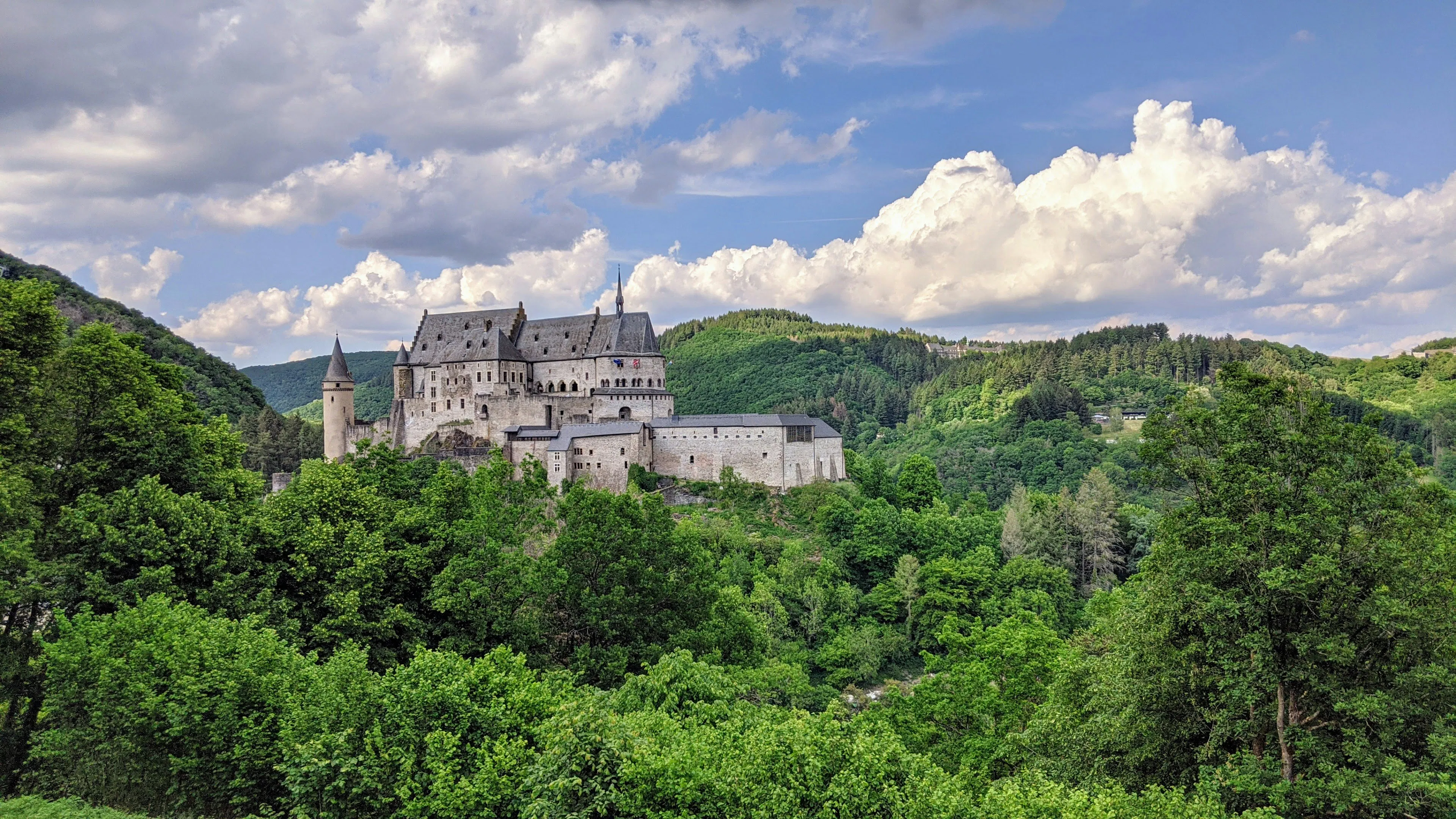 Stone castle on a wooded hillside in Luxembourg under a partly cloudy sky.
