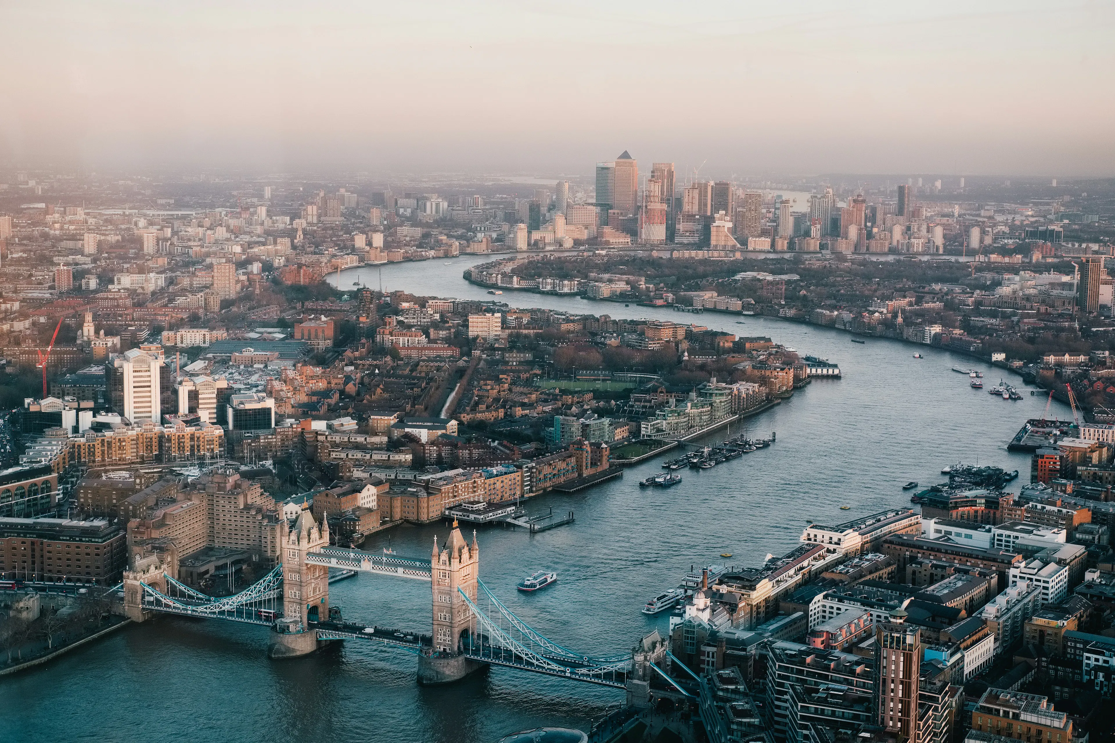 Aerial view of Tower Bridge and the River Thames winding through London with the city skyline in the distance.