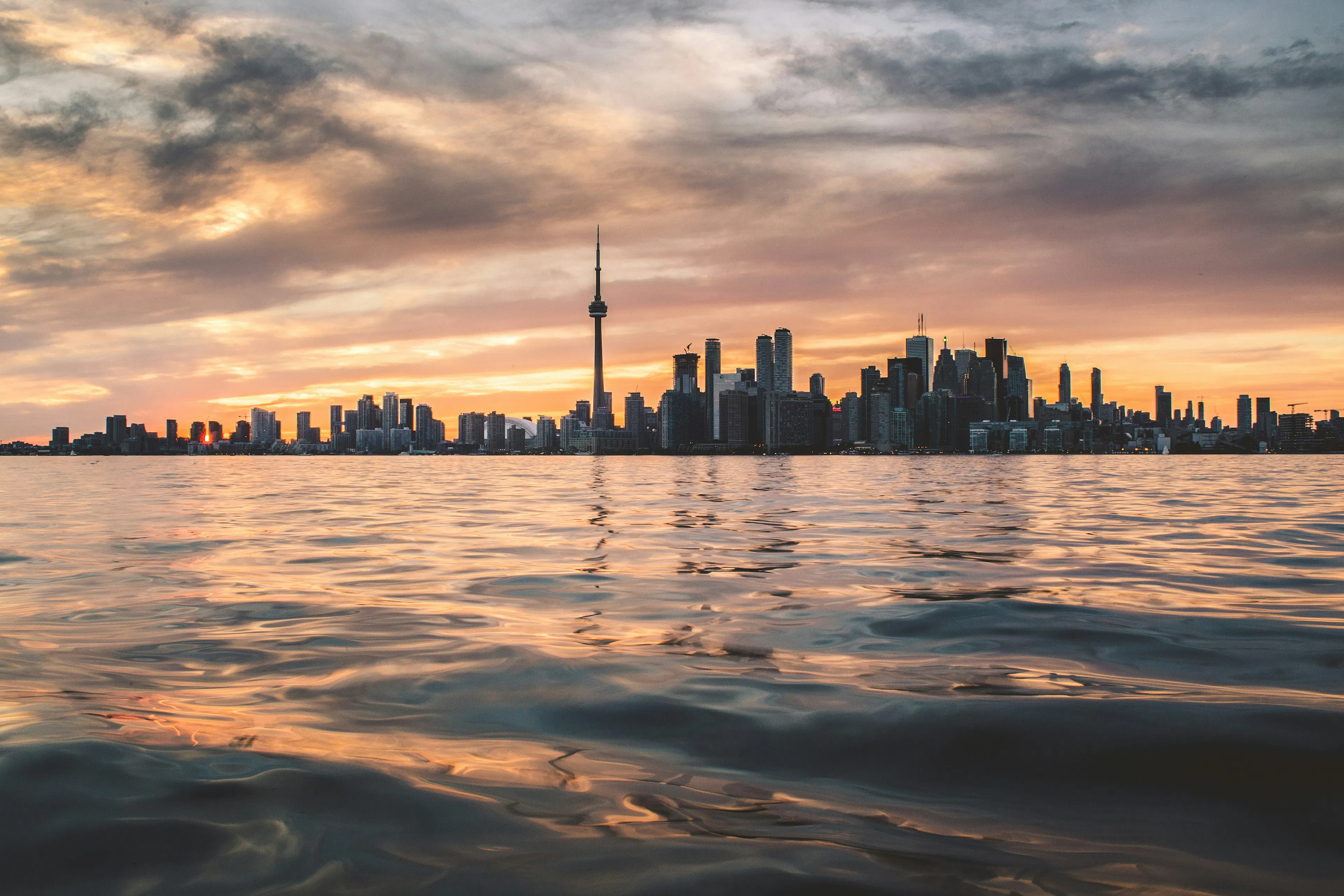 Toronto skyline at sunset with the CN Tower reflected across the water.