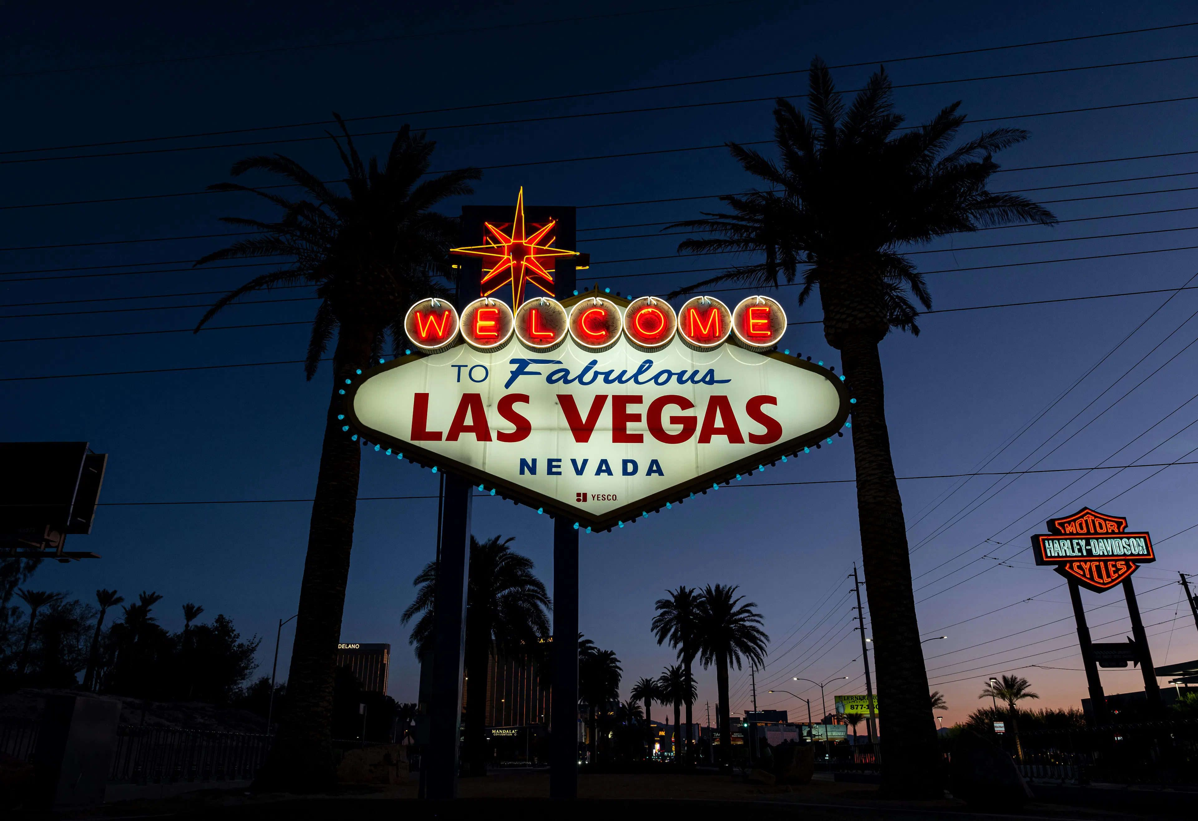 Welcome to Fabulous Las Vegas Nevada sign illuminated at dusk with palm trees and roadside lights in the background.