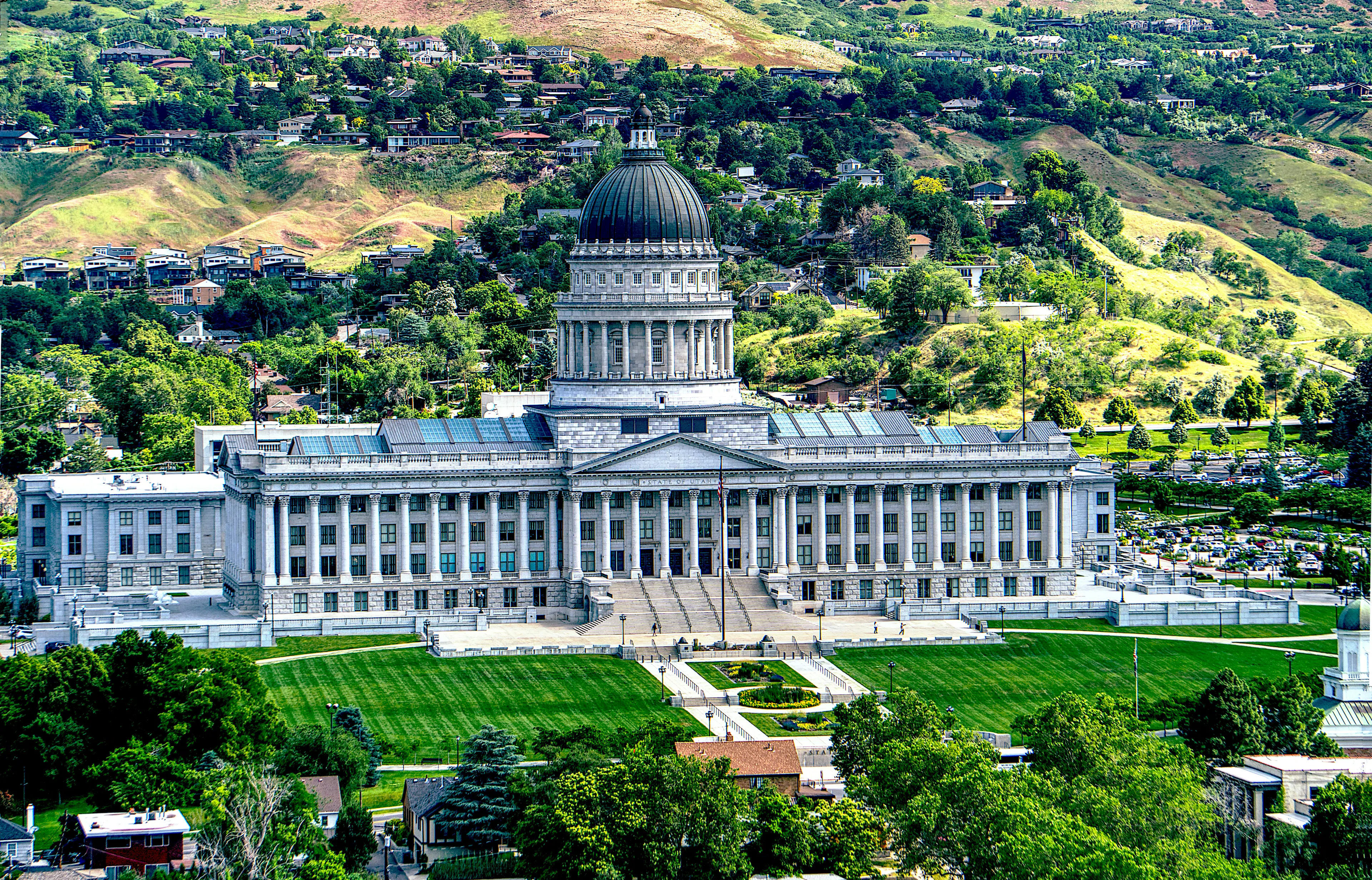 Utah State Capitol building with a large central dome, landscaped lawns, and hillside neighborhoods in the background.