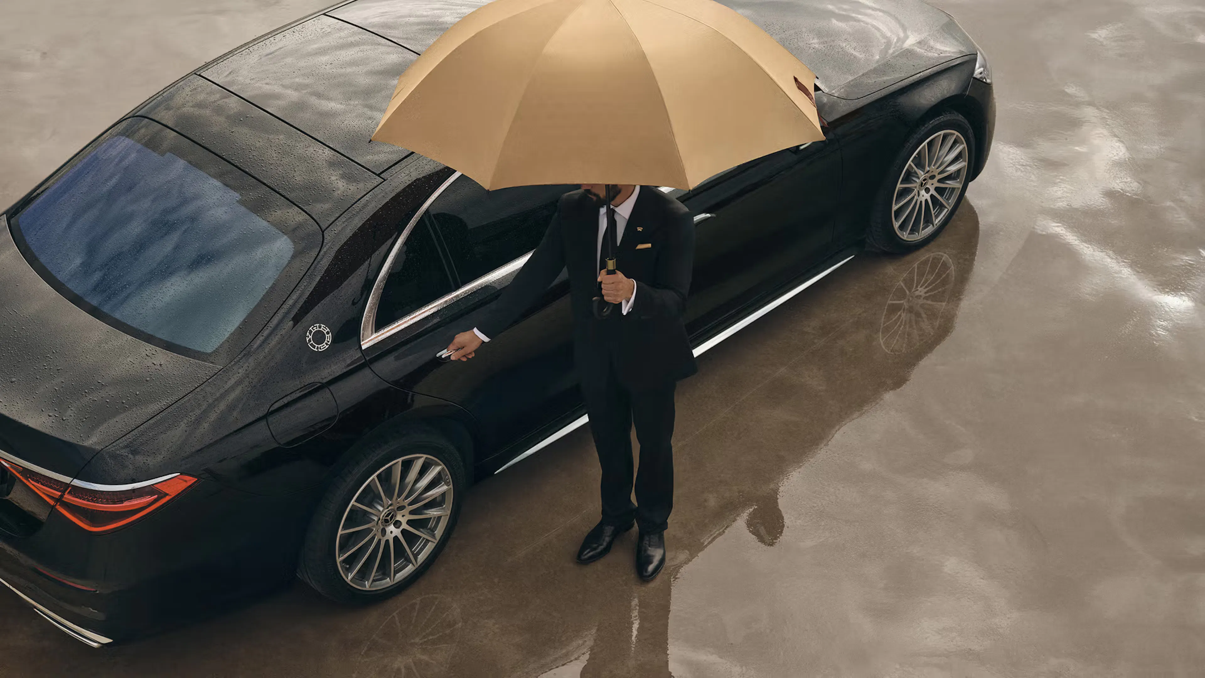 Luxury sedan with a chauffeur holding an umbrella beside the vehicle.