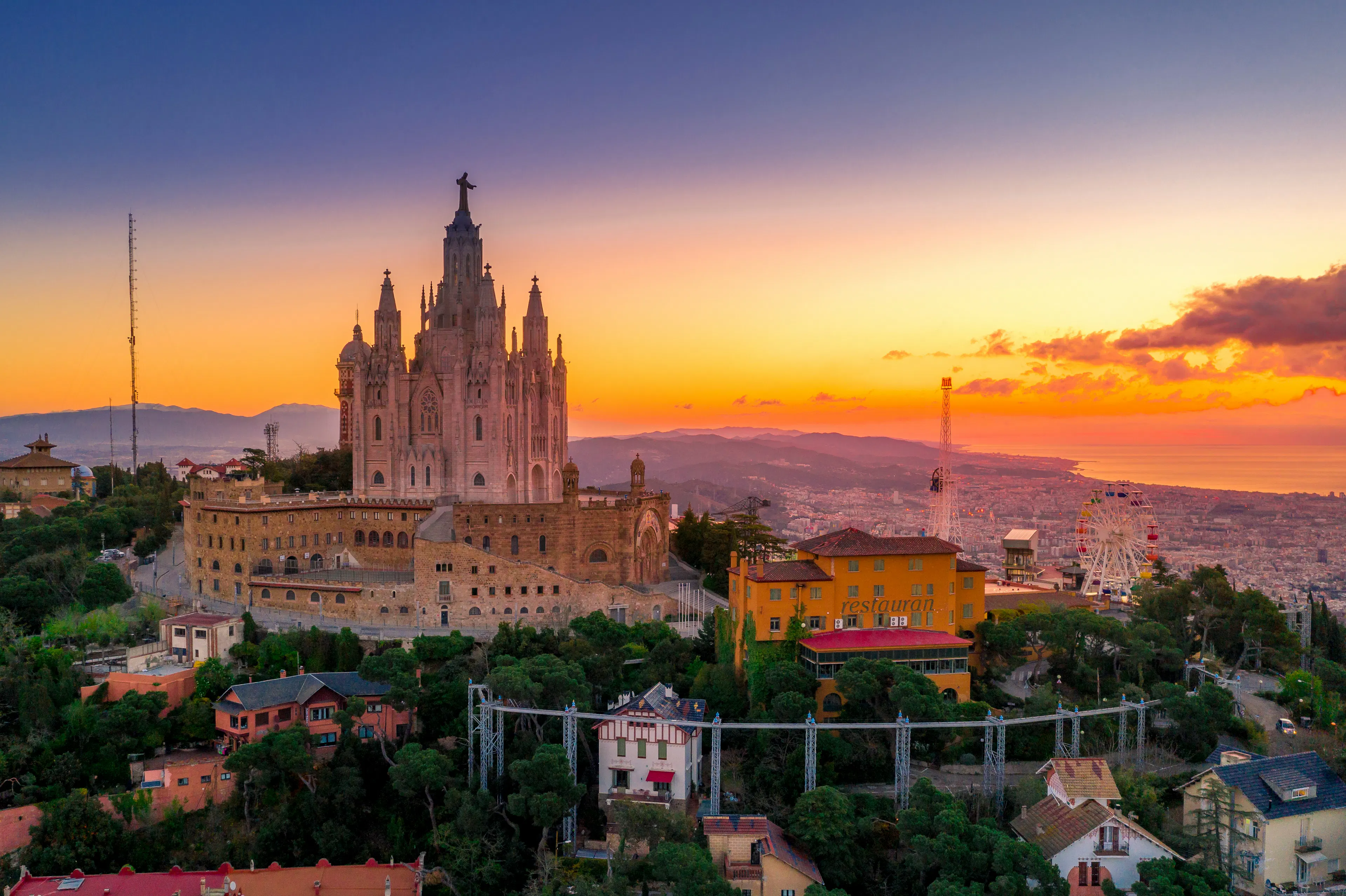 The Temple of the Sacred Heart atop Tibidabo Hill overlooking Barcelona at sunset, with sweeping views of the city and Mediterranean coastline.