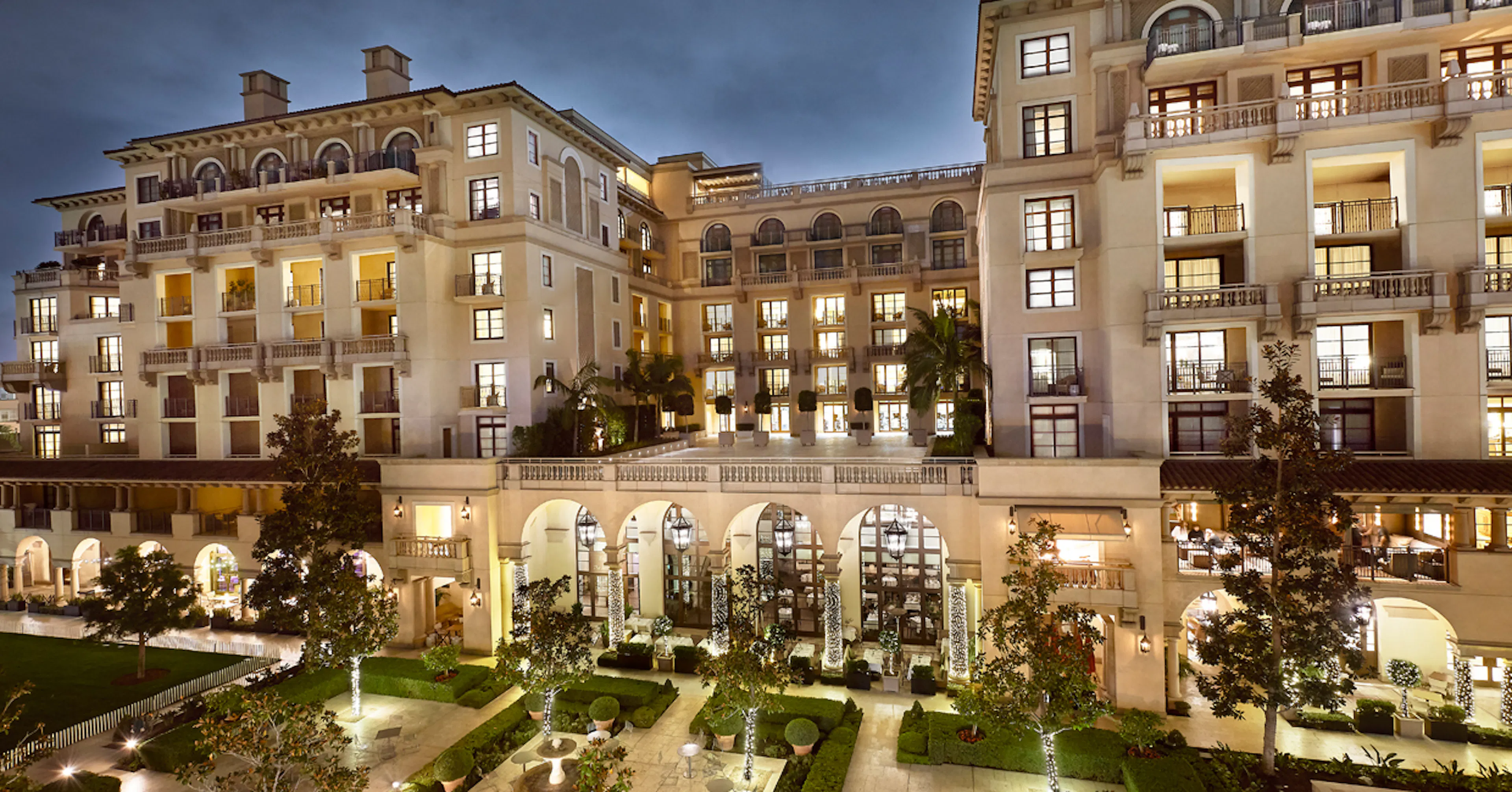 Illuminated luxury hotel exterior with landscaped courtyard at dusk.