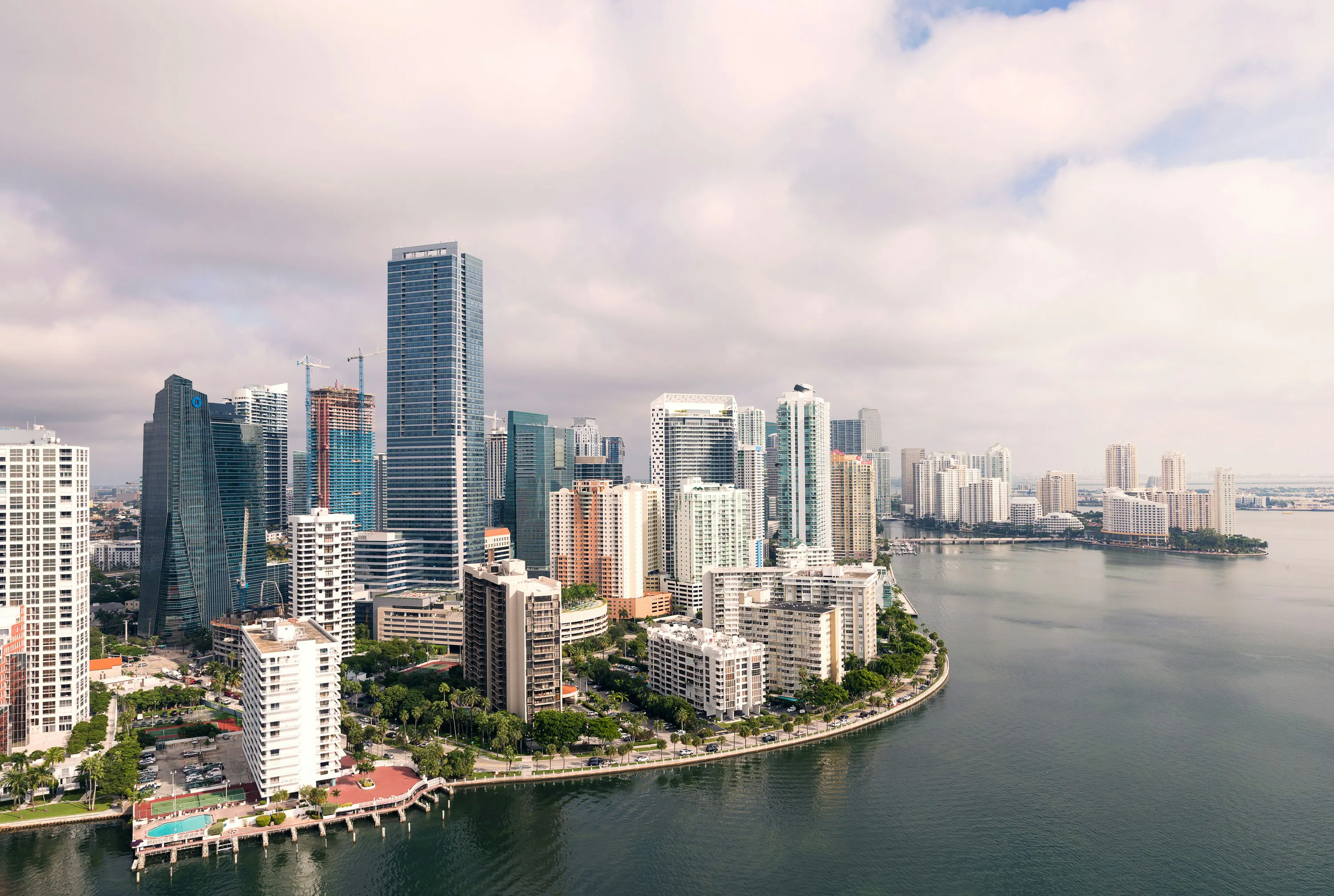 Aerial view of downtown Miami and Brickell with waterfront high-rise buildings along Biscayne Bay under cloudy skies.