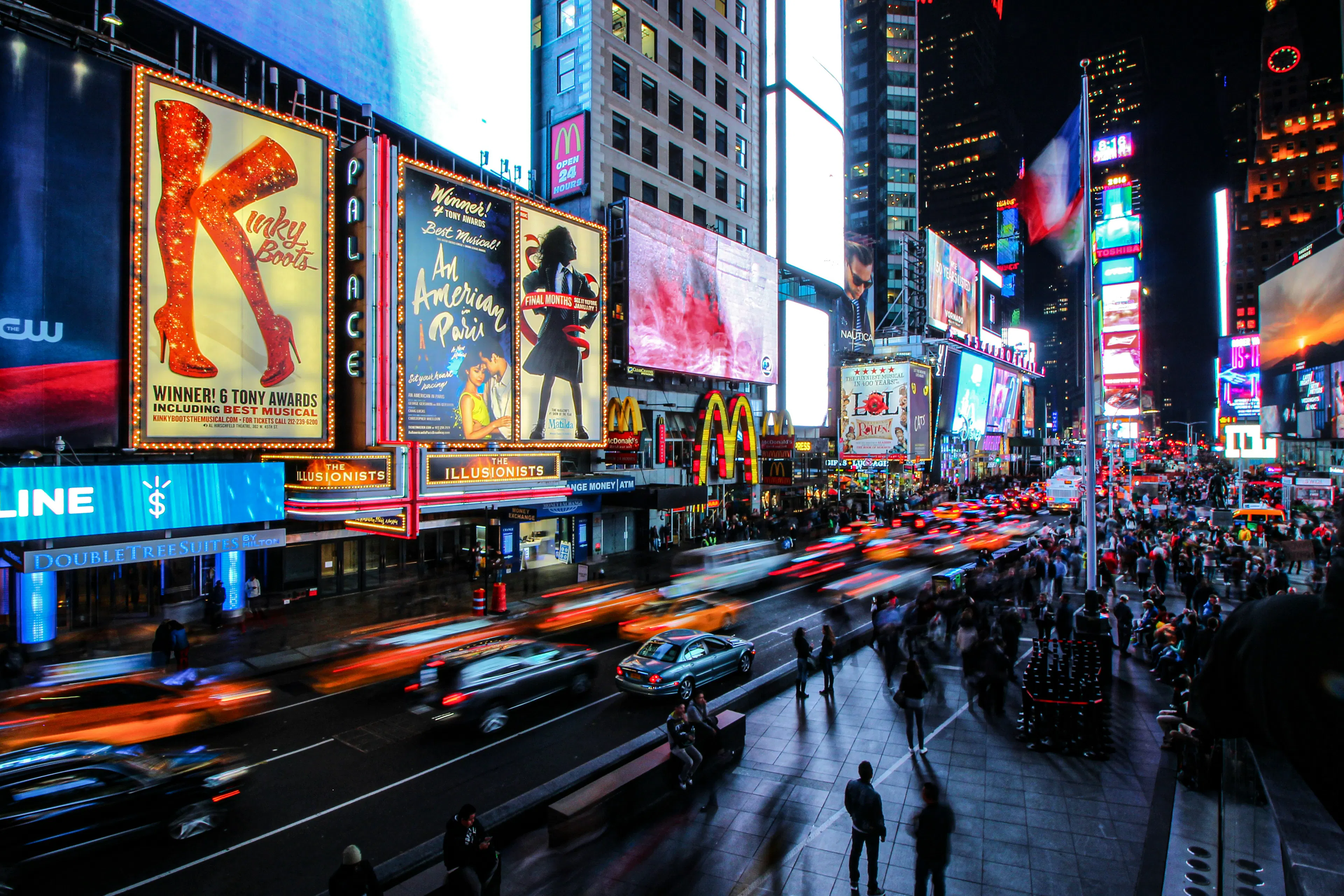 Times Square at night with illuminated billboards, traffic, and crowds along the street.