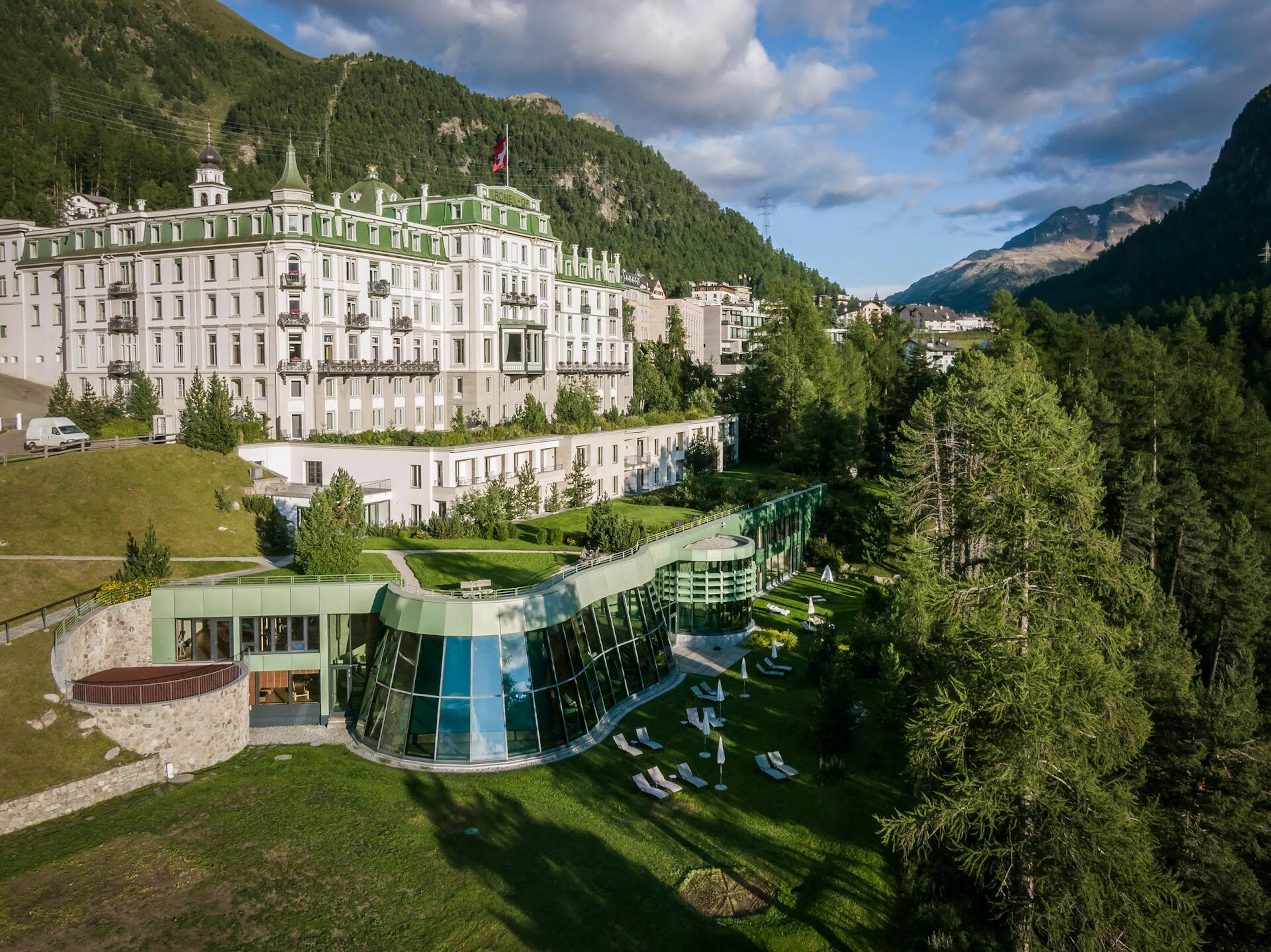 Grand mountain hotel surrounded by lush greenery and alpine scenery.