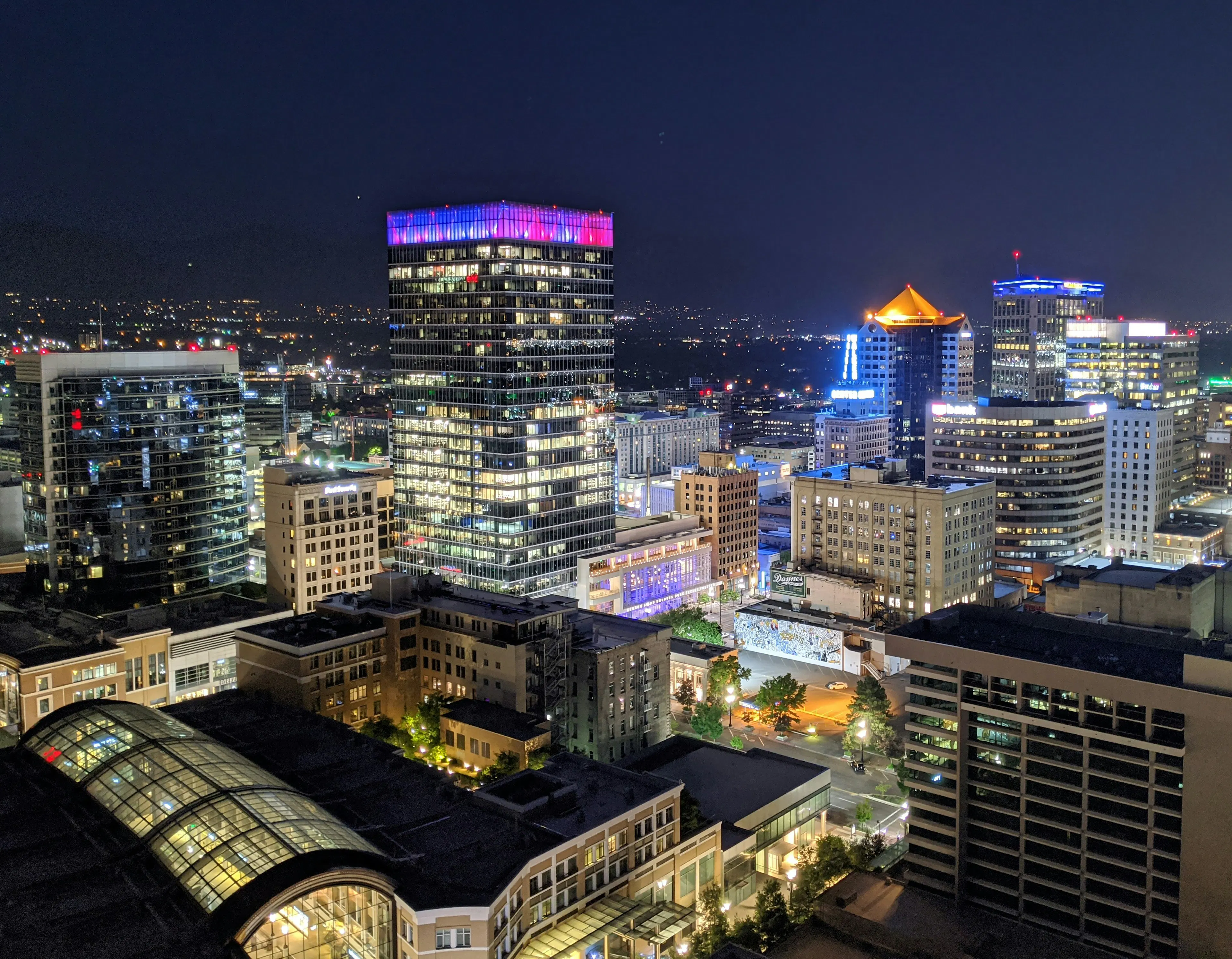 Salt Lake City skyline at night with illuminated office towers, city streets, and mountain foothills in the distance.
