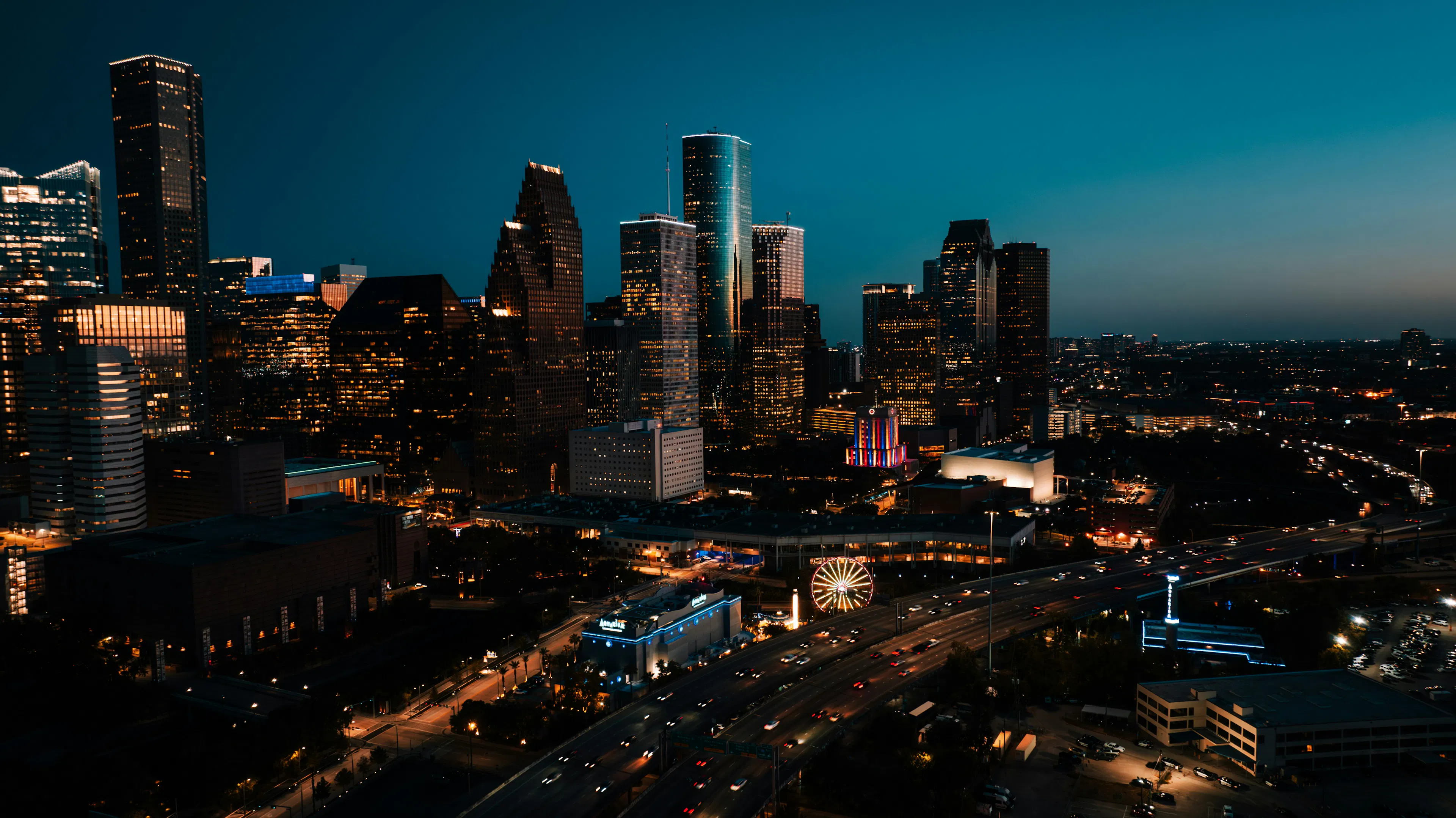 Downtown Houston skyline at night with illuminated high-rise buildings, highways, and city lights.