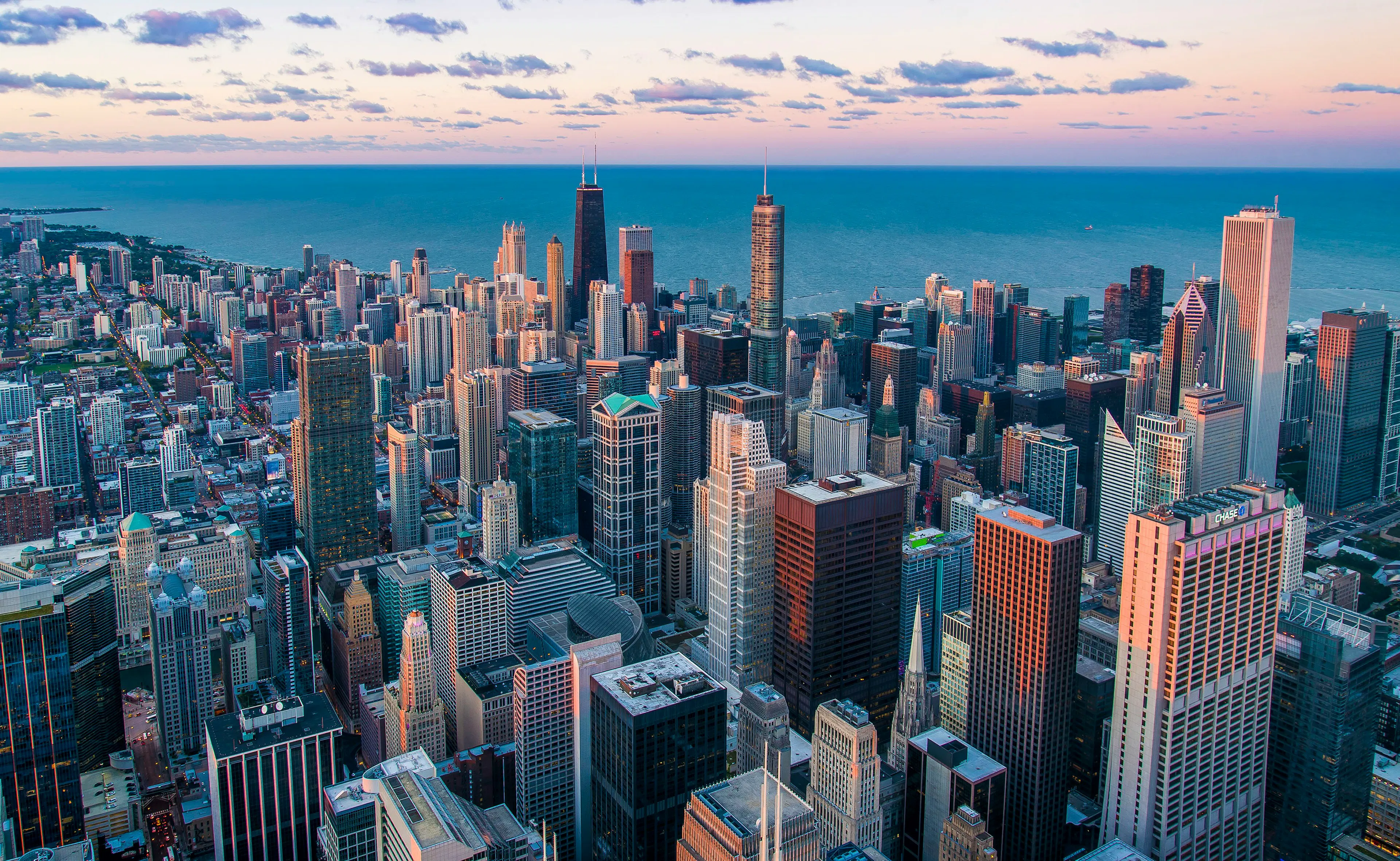 Aerial view of downtown Chicago with high-rise buildings along Lake Michigan under a partly cloudy sky.