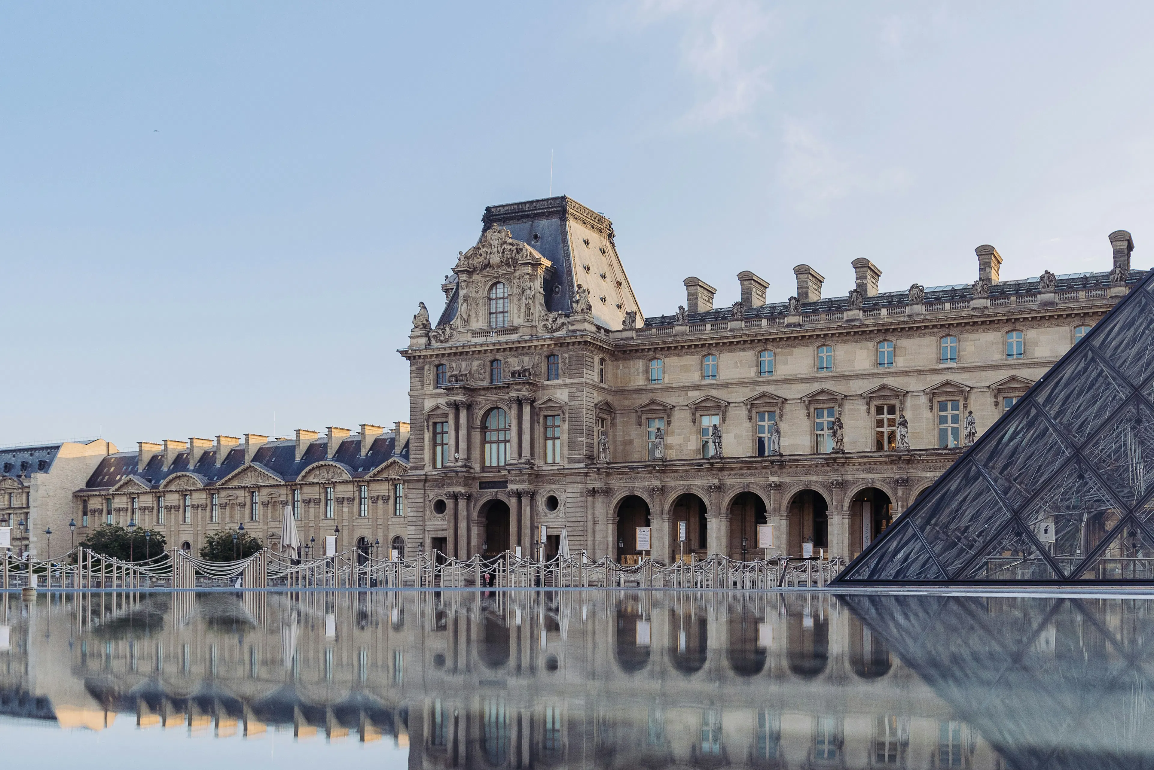 Glass pyramid at the Louvre Museum with historic palace buildings reflected in a calm pool.