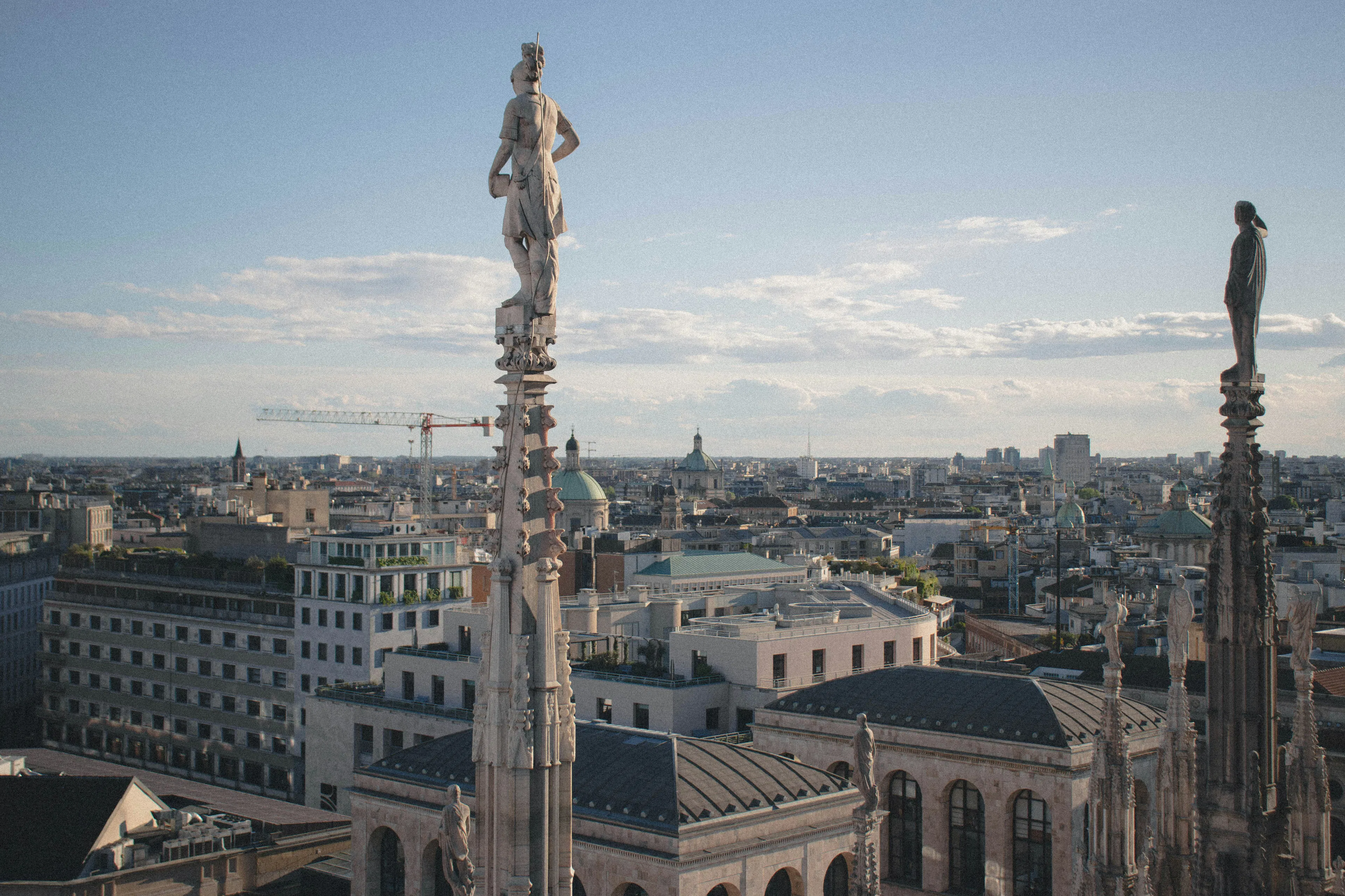 View of Milan from the rooftop of the Duomo di Milano, featuring ornate Gothic spires and statues overlooking the city skyline.