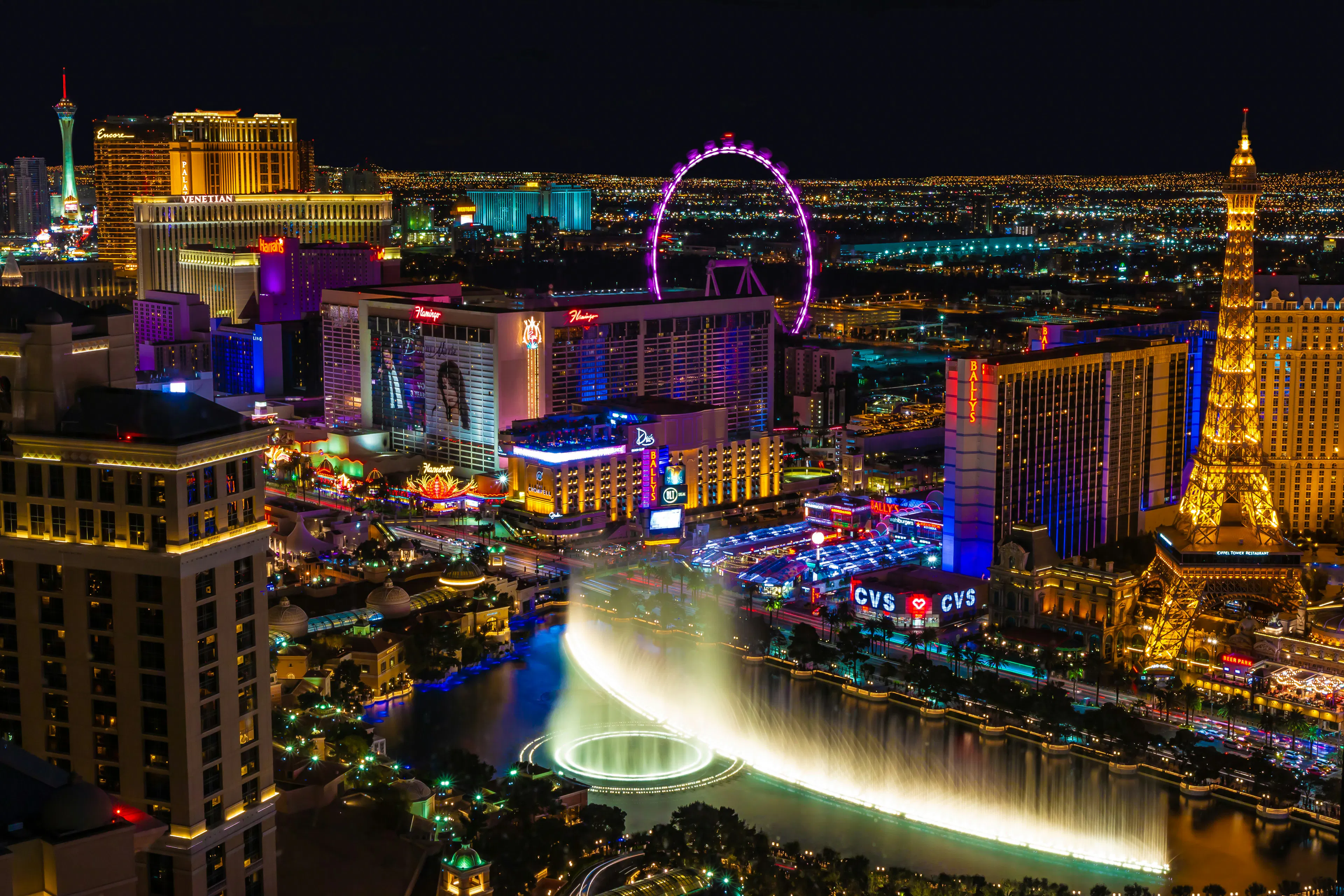 Las Vegas Strip at night with illuminated hotels, the High Roller observation wheel, and Bellagio fountains.