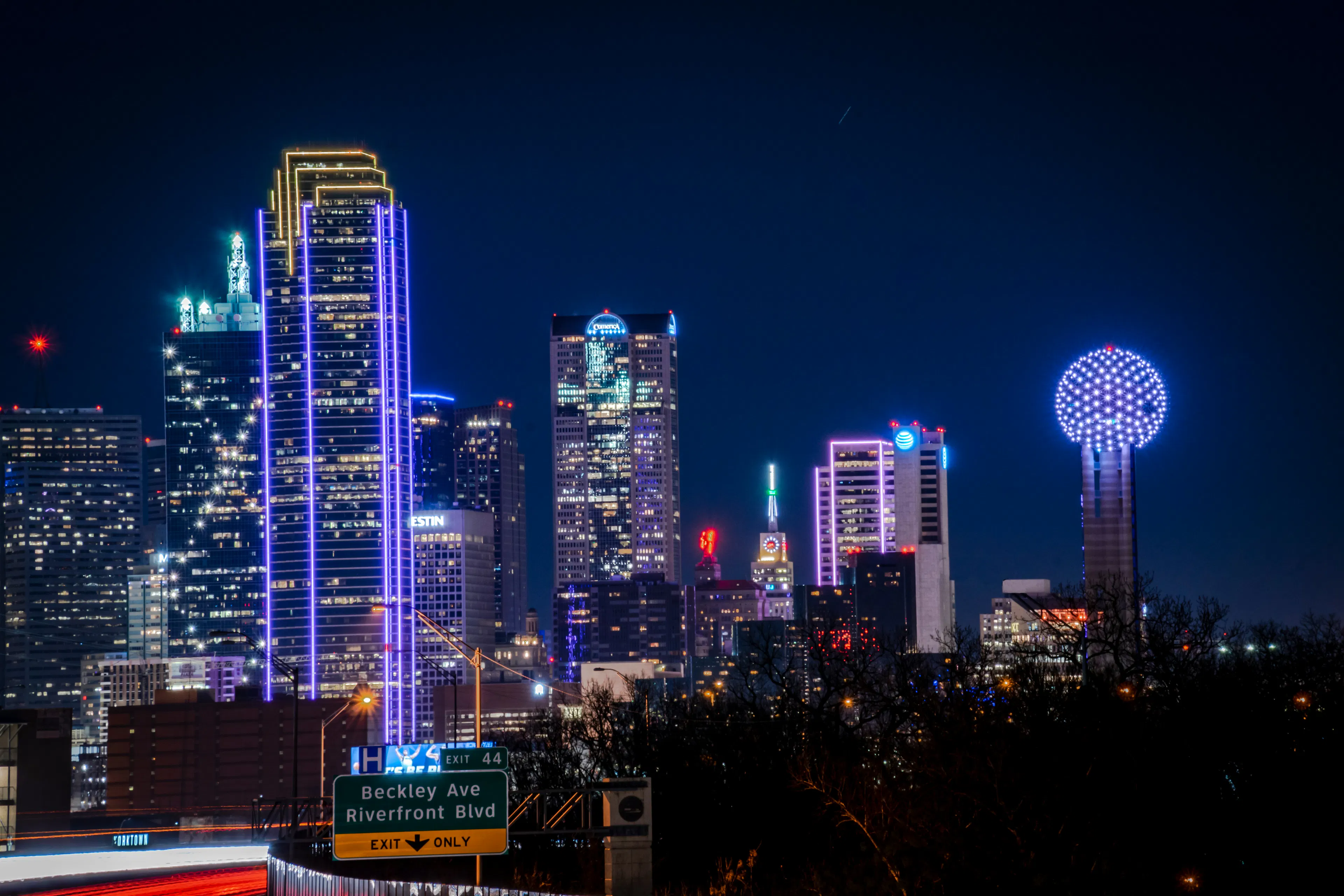 Dallas skyline at night with illuminated skyscrapers and Reunion Tower lit against a dark sky.