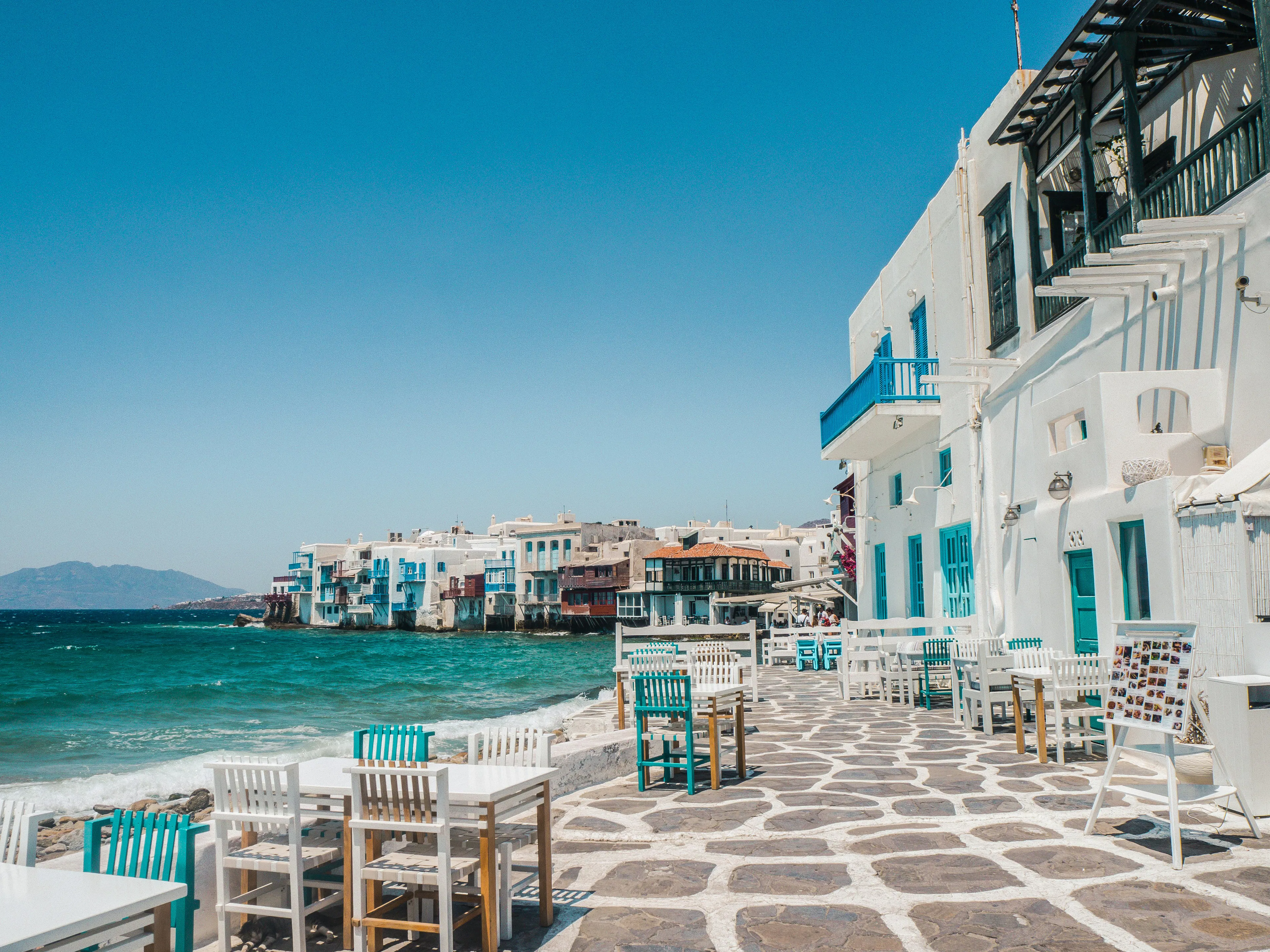 Seaside cafés and whitewashed buildings lining the waterfront, overlooking the turquoise waters of the Aegean Sea.