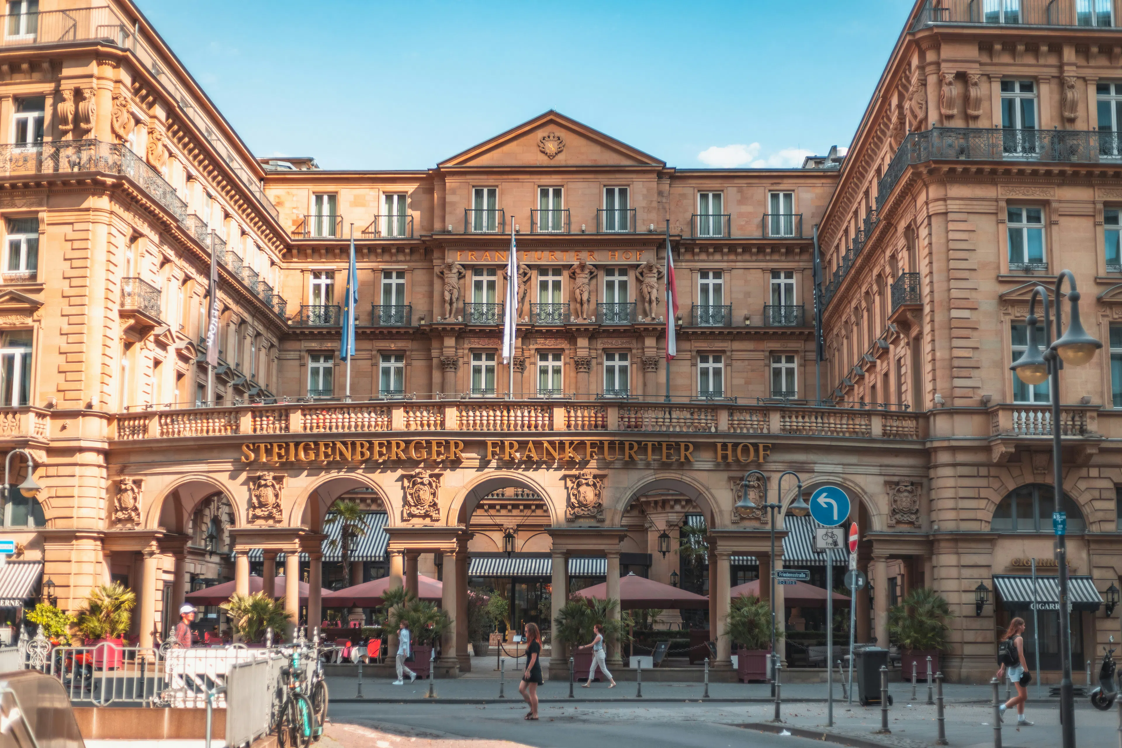 Steigenberger Frankfurter Hof hotel facade with arched entrances, balconies, flags, and pedestrians along the street.