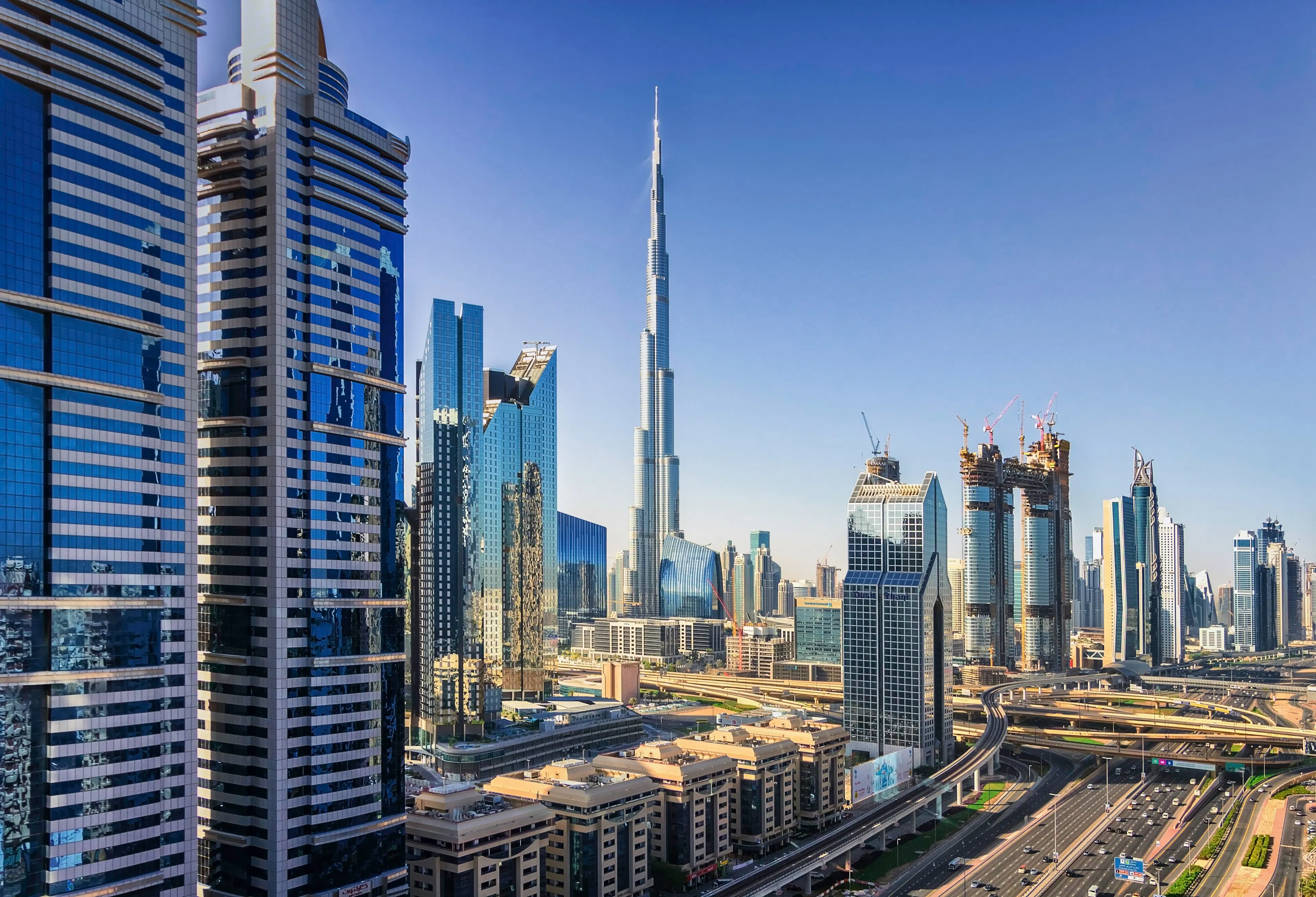 Dubai skyline with the Burj Khalifa rising above surrounding high-rise buildings and elevated roads during daytime.