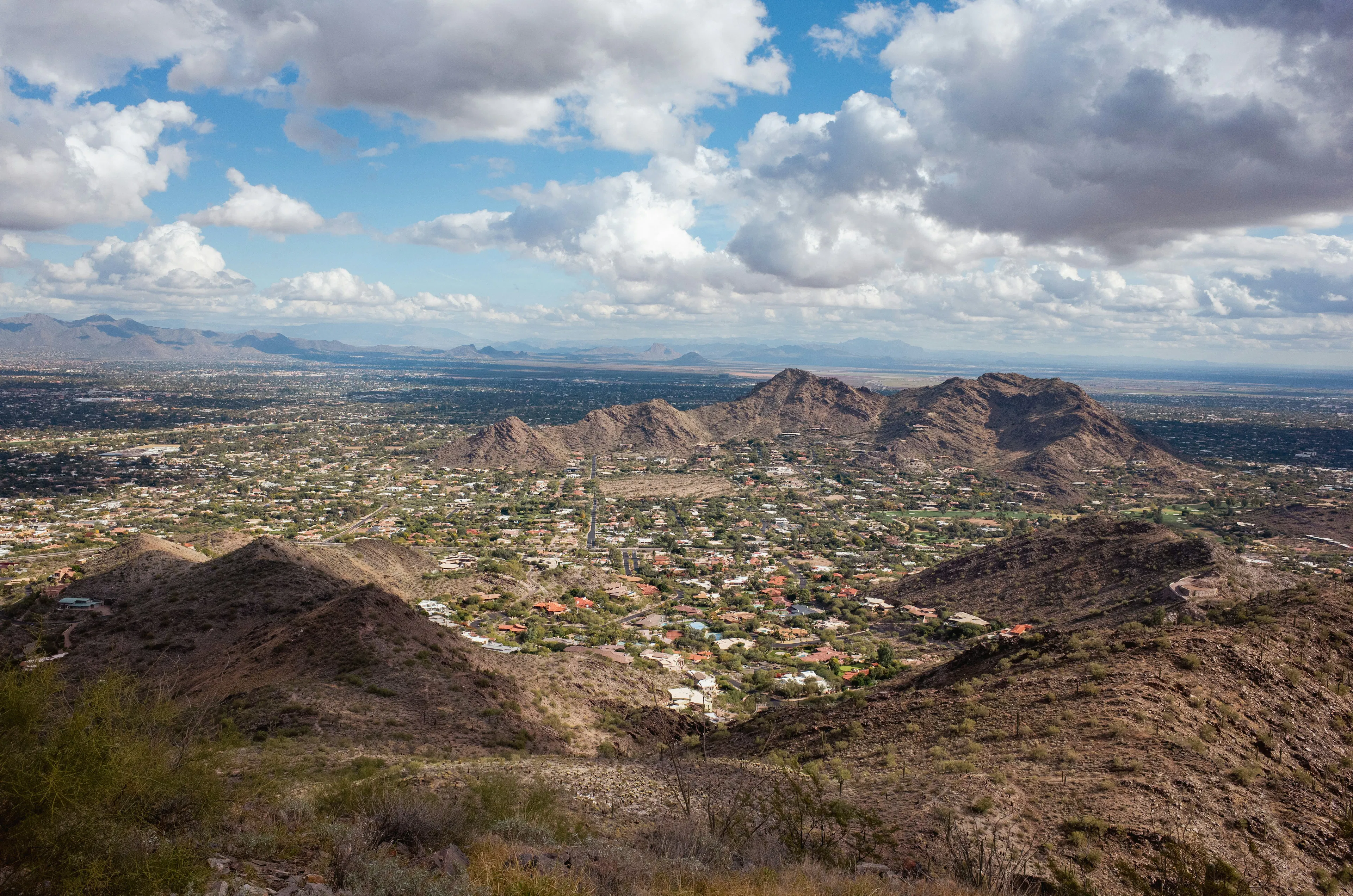 Desert landscape near Scottsdale with rocky hills, residential neighborhoods, and distant mountain ranges beneath dramatic clouds.