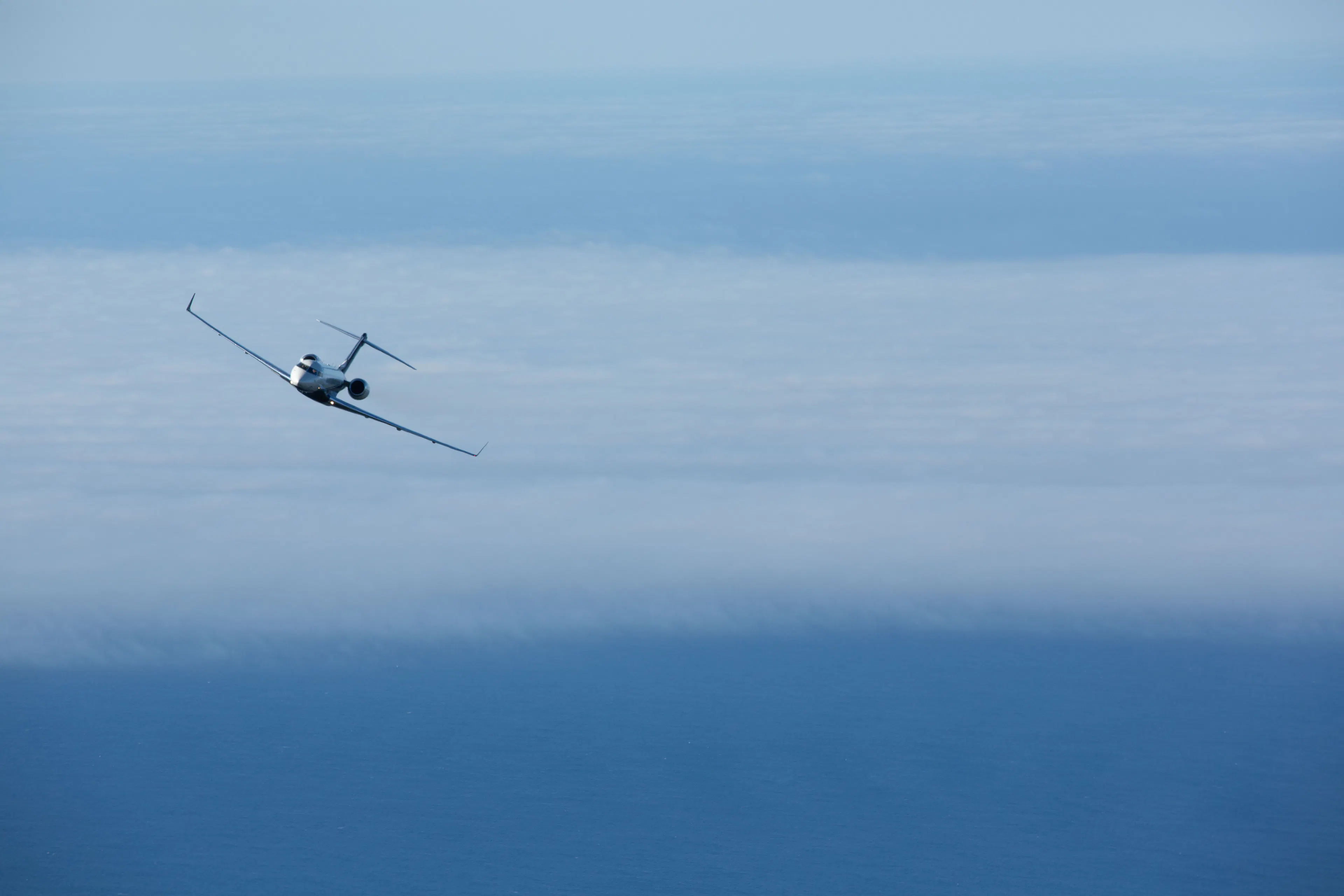A private jet flying above a blanket of clouds, surrounded by expansive blue skies and ocean views.