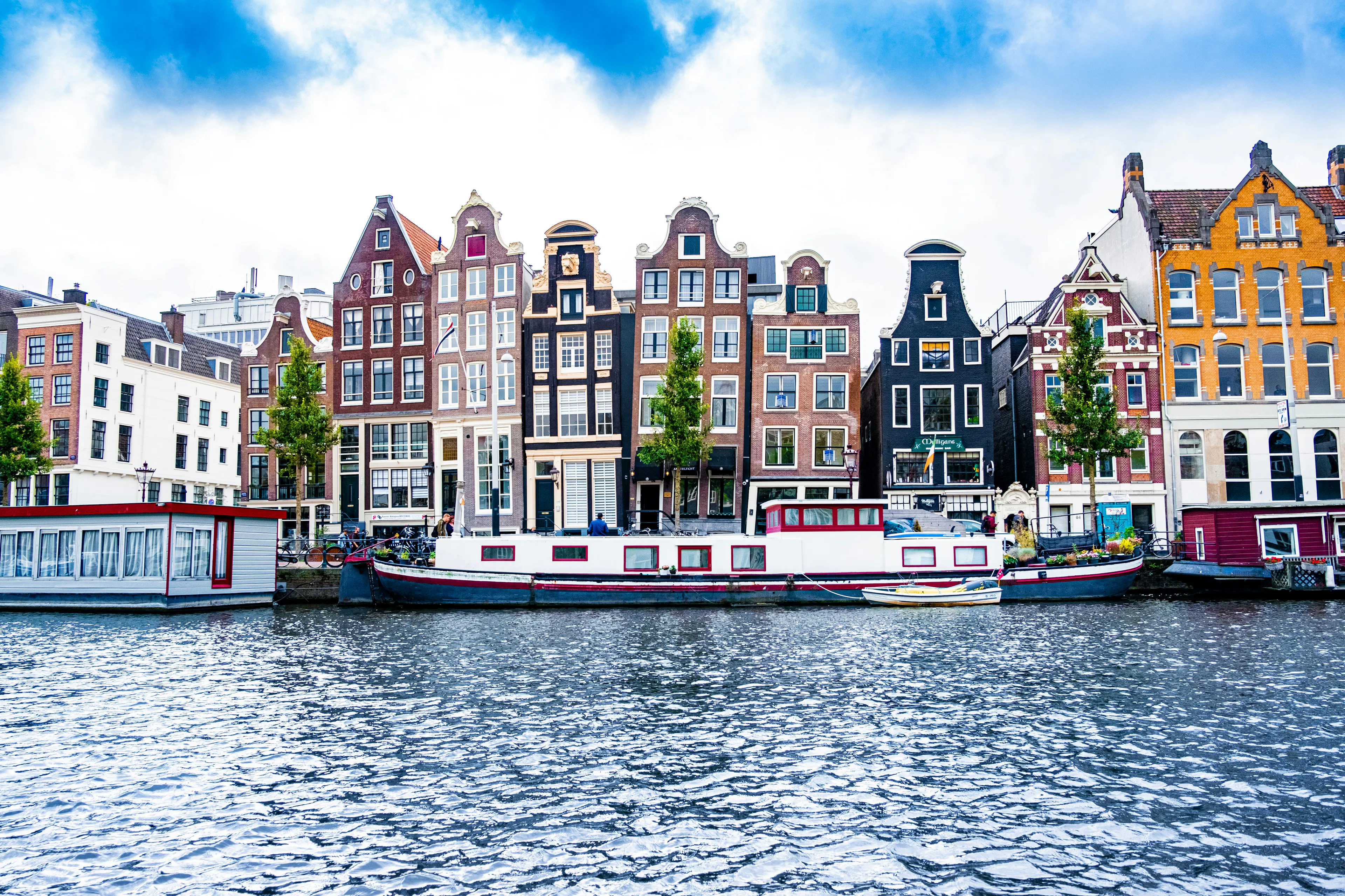 Colorful historic canal houses lining an Amsterdam waterway, with boats docked along the waterfront.