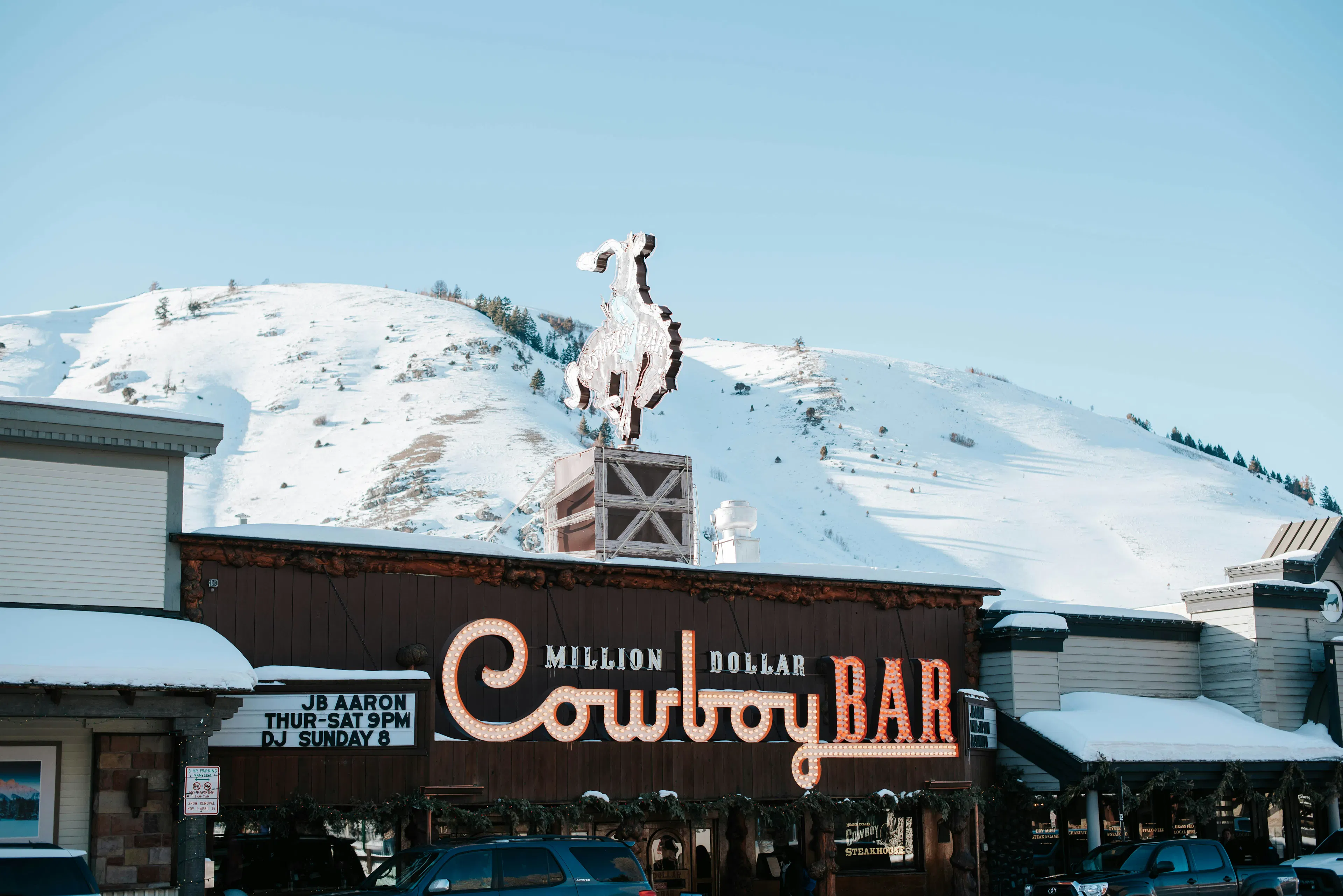 Million Dollar Cowboy Bar in Jackson Hole with snow-covered hills and a bucking horse sign above the building.