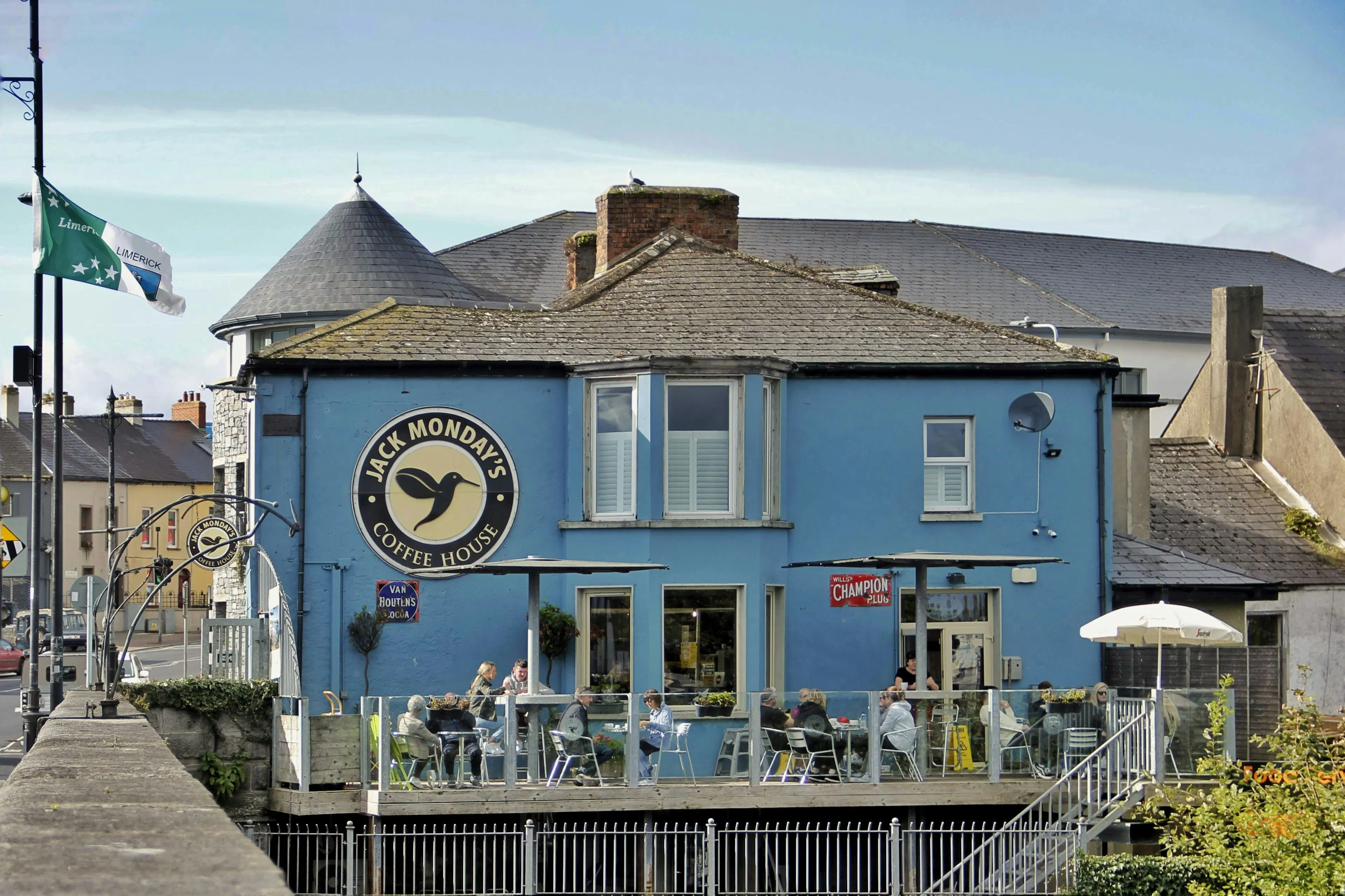 Blue waterfront café building with outdoor seating and visitors along a riverside walkway in Limerick.