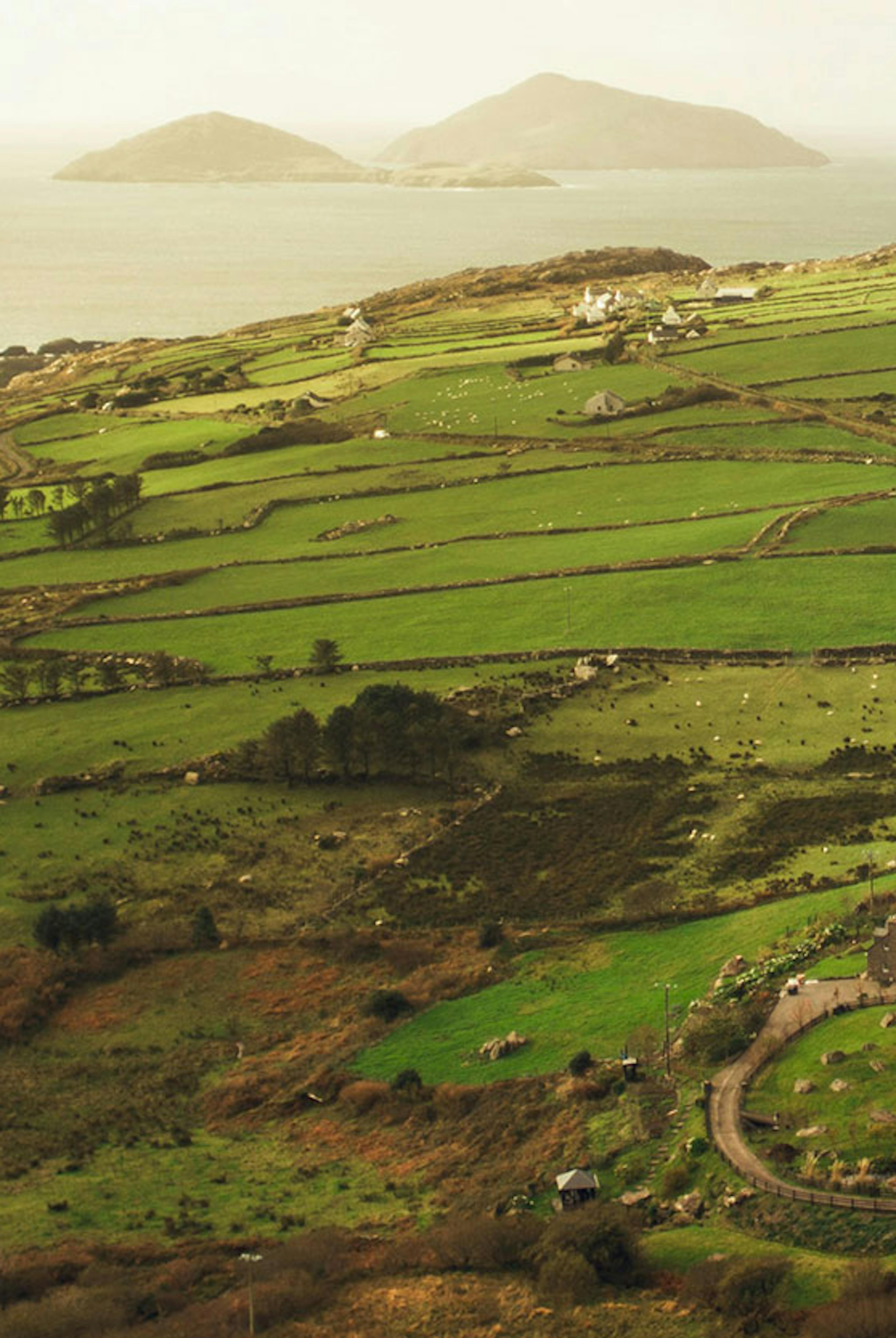 An expanse of green fields reach out to waters with islands on the horizon