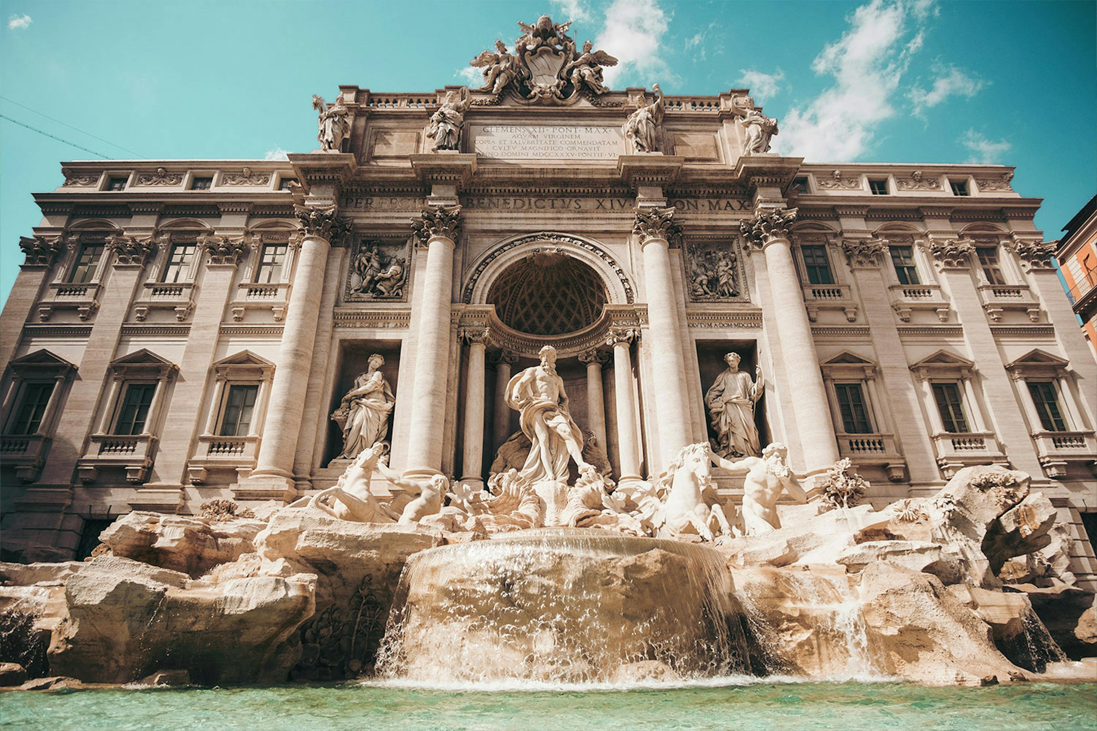 ornate statues adorn the lip of a fountain outside a beautiful building