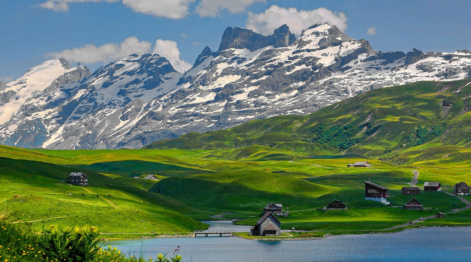 Tra le montagne che dominano la scena, un’ampia distesa verde accoglie eleganti residenze affacciate sul lago.