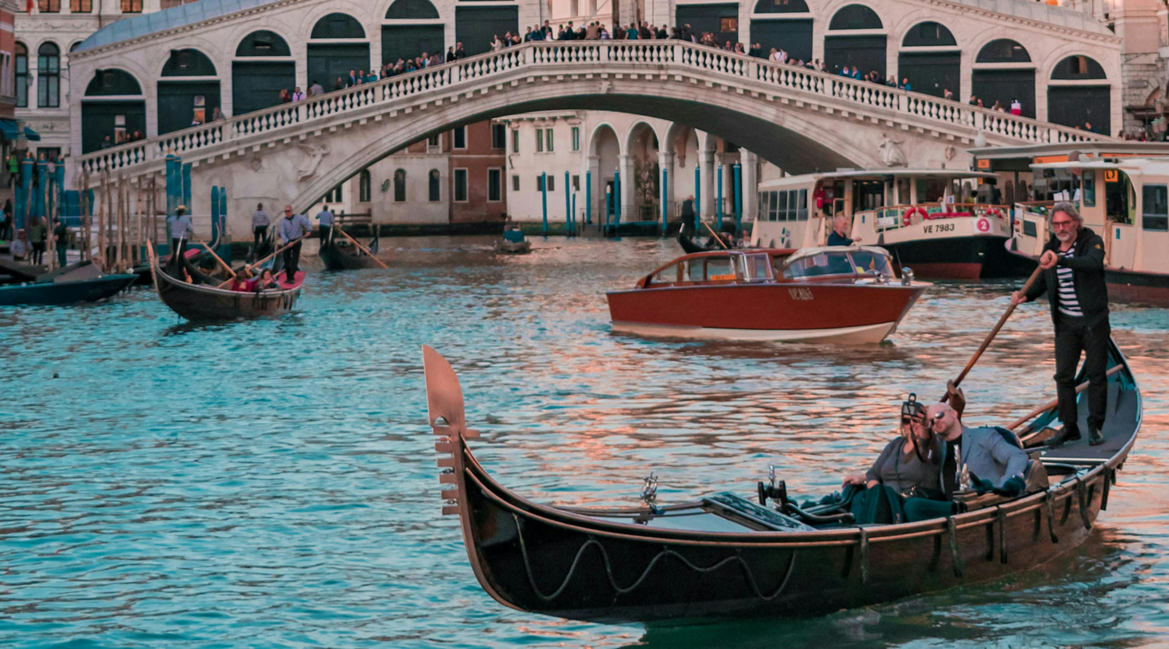 Italian boats float the river with a bridge in the background