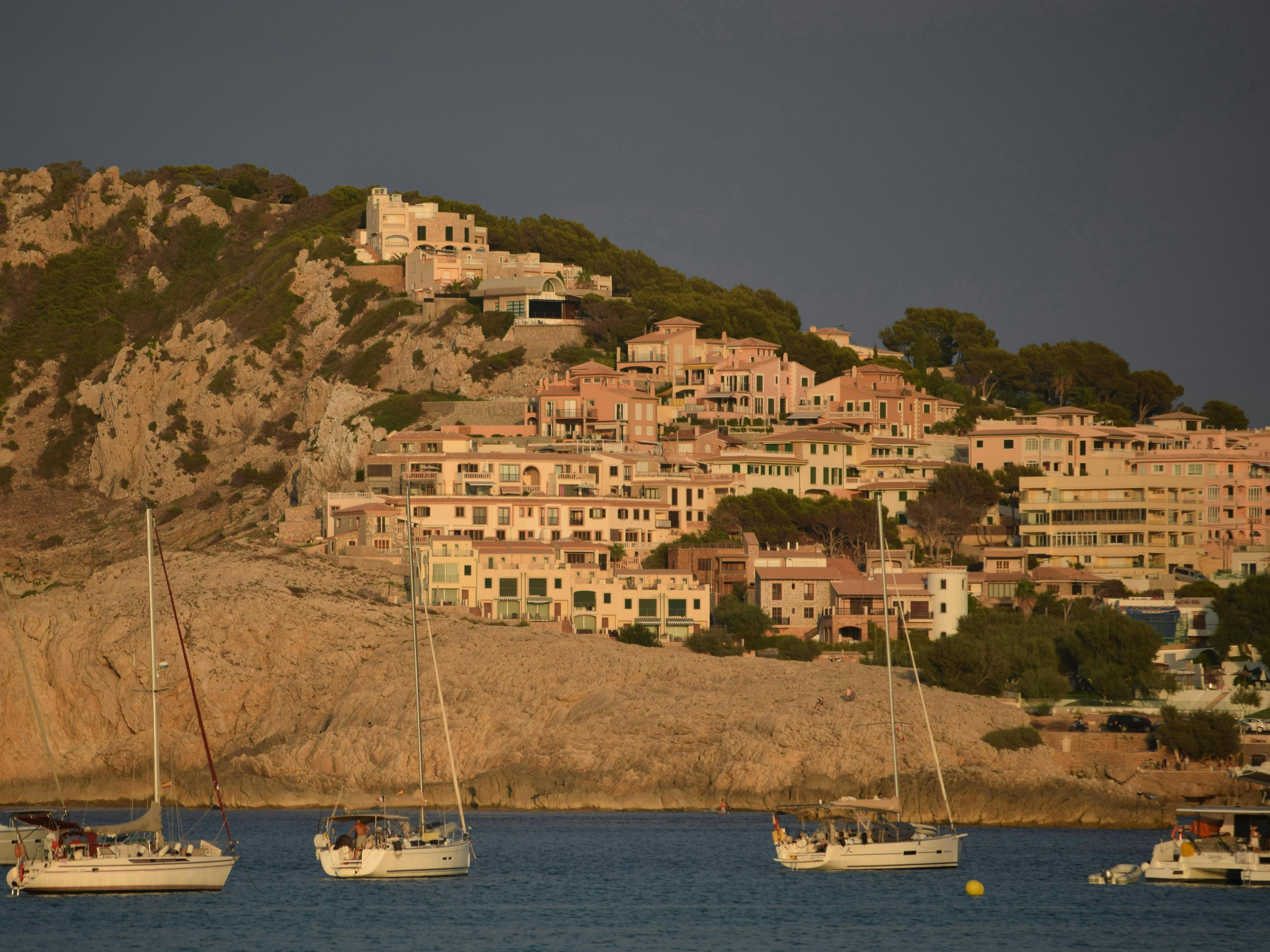 boats in the bay by a ridge of mountain that has a cluster of houses at its feet
