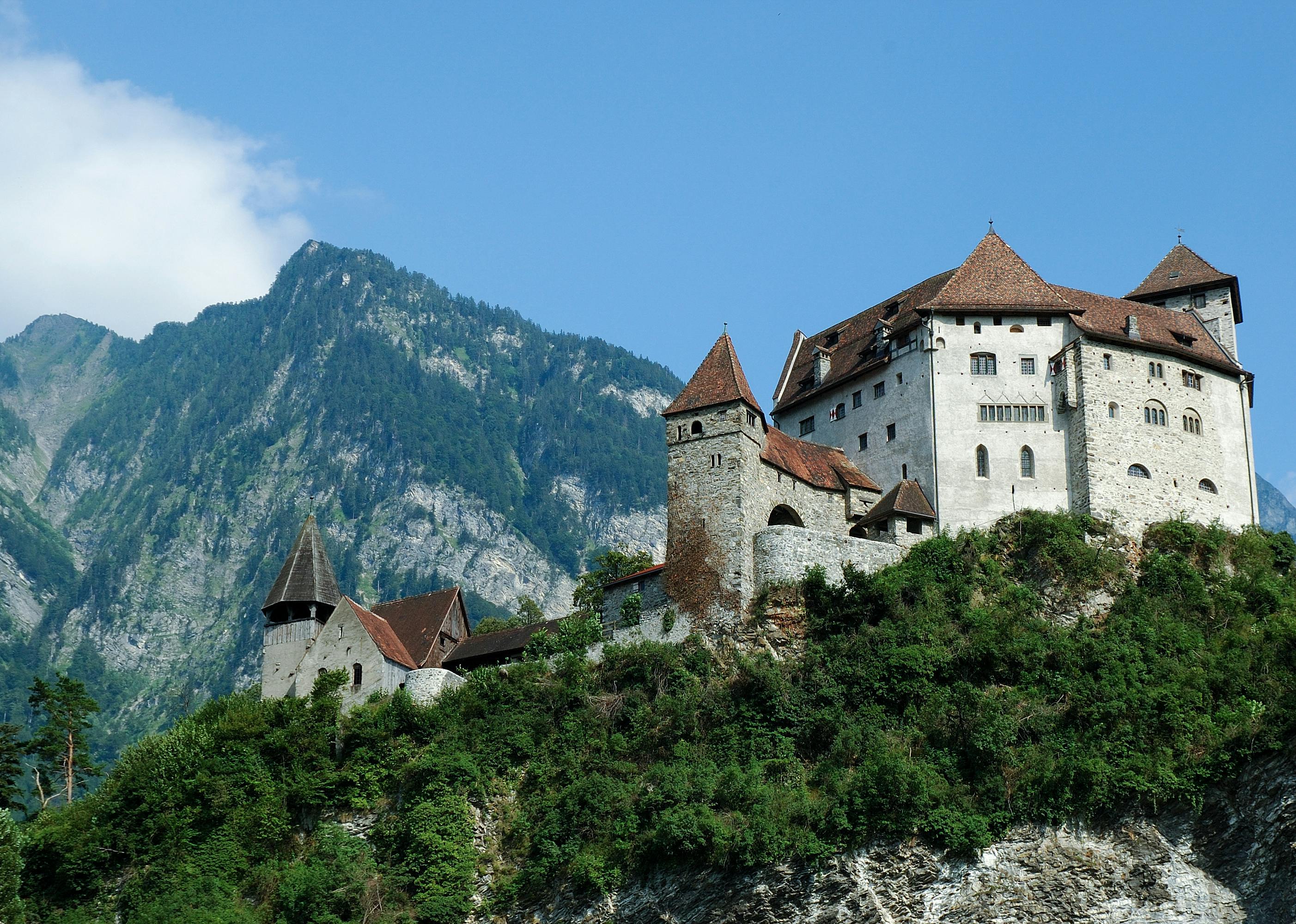 Castle structure on top part of a mountain with a peak of a higher elevation in the background