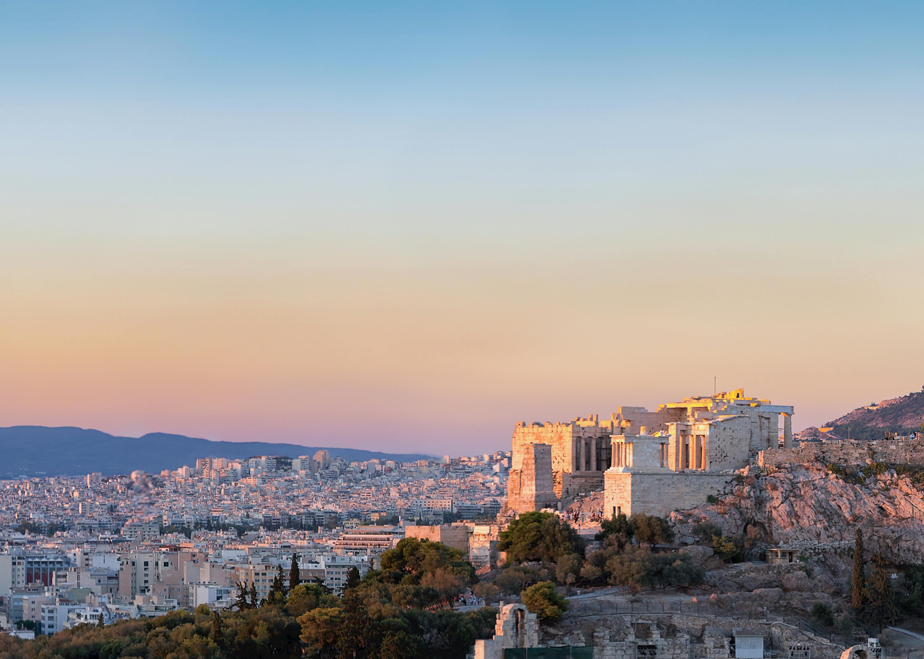 Castle structure sits on top of a mountain with a view of the city in the valley and another mountain on the horizon