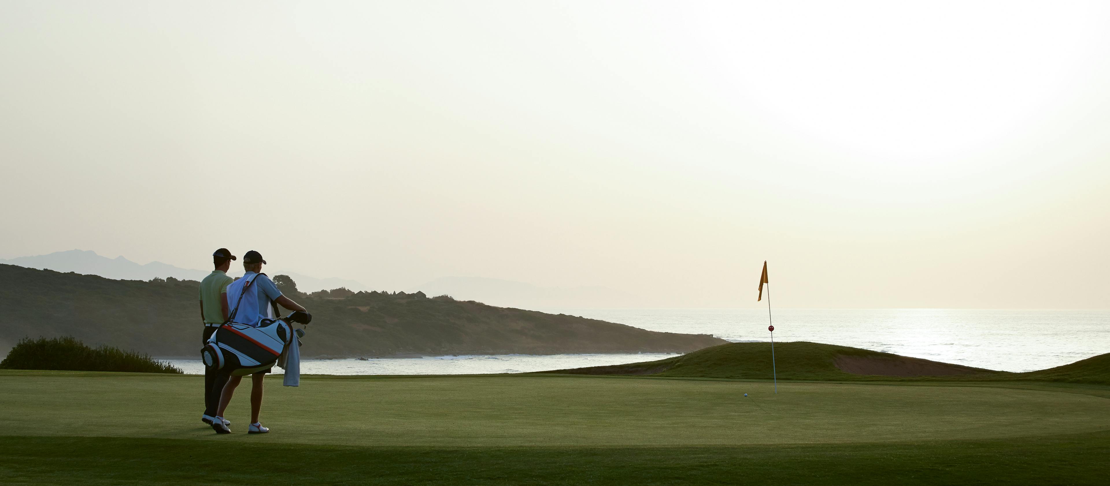 A couple of golfers look out over the green at a pin