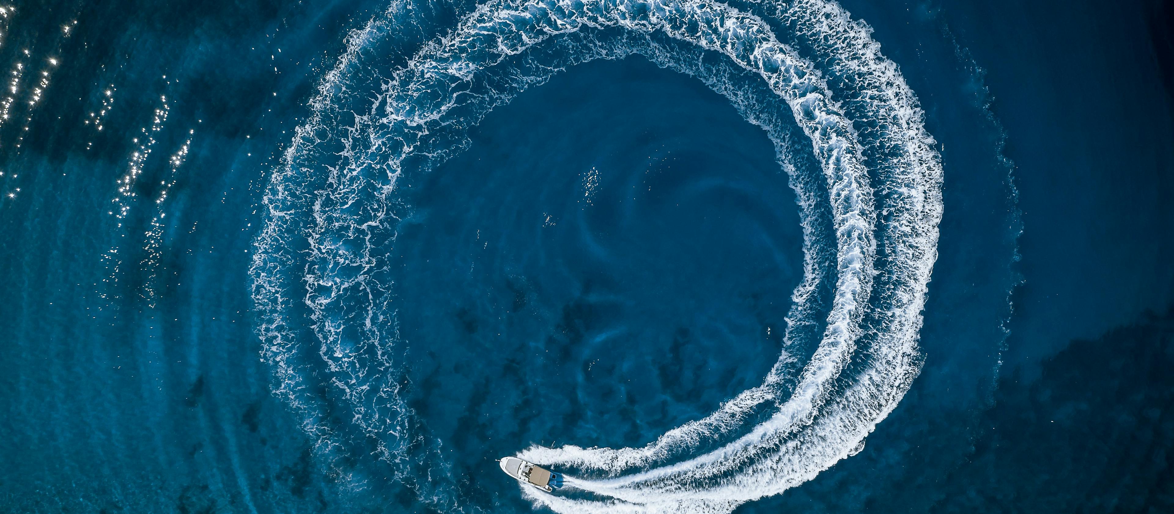 Overhead shot of a boat on beautiful blue water performing a circle in the waves